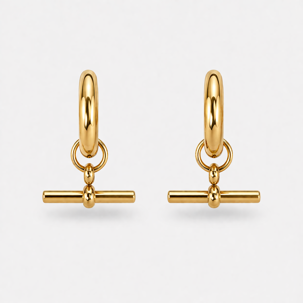Pair of gold hoop earrings with bar charms on a light gray background