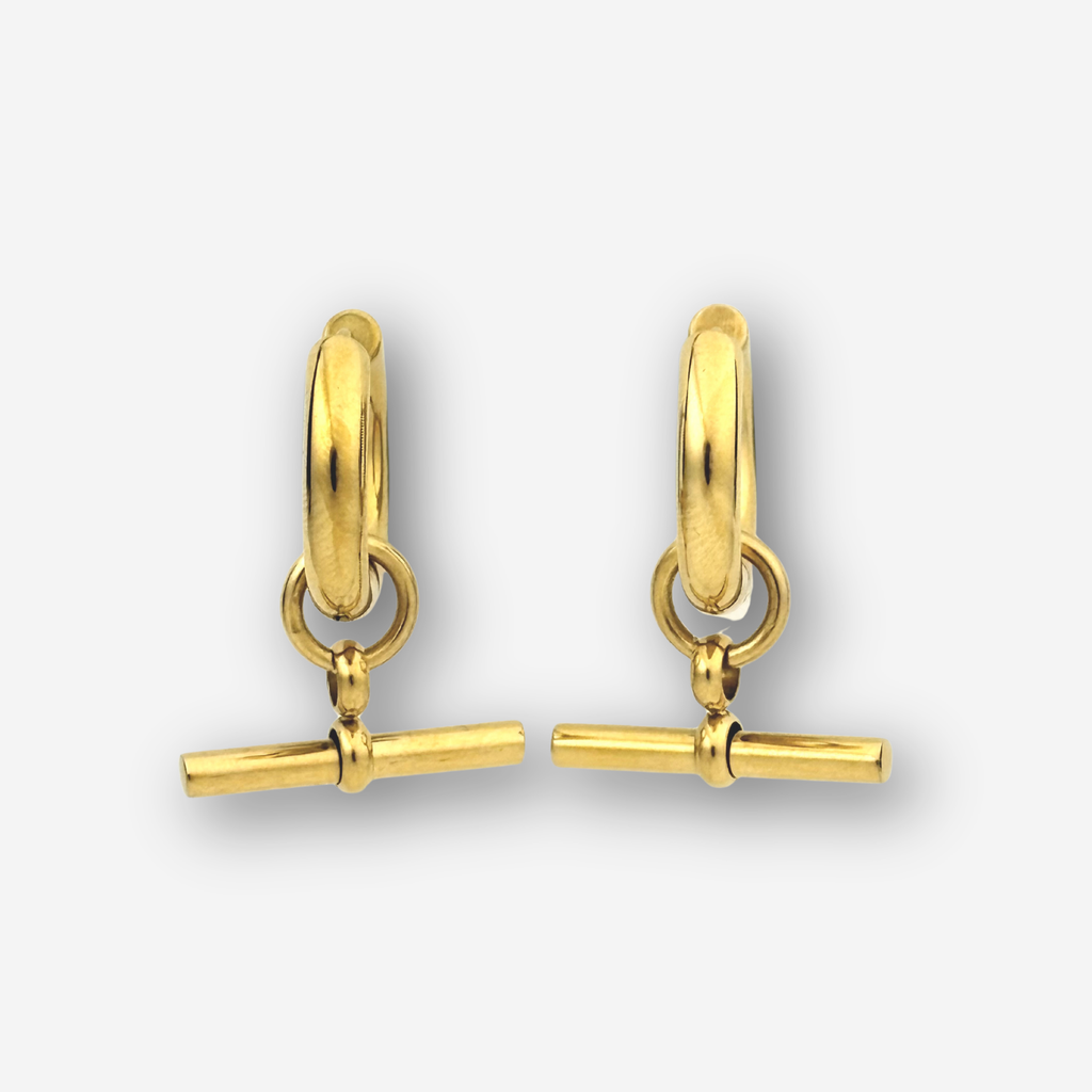 A pair of gold huggie hoop earrings with a toggle bar charm, shown on a light gray background.