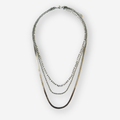 A layered necklace featuring three distinct chain styles in silver against a light gray background.