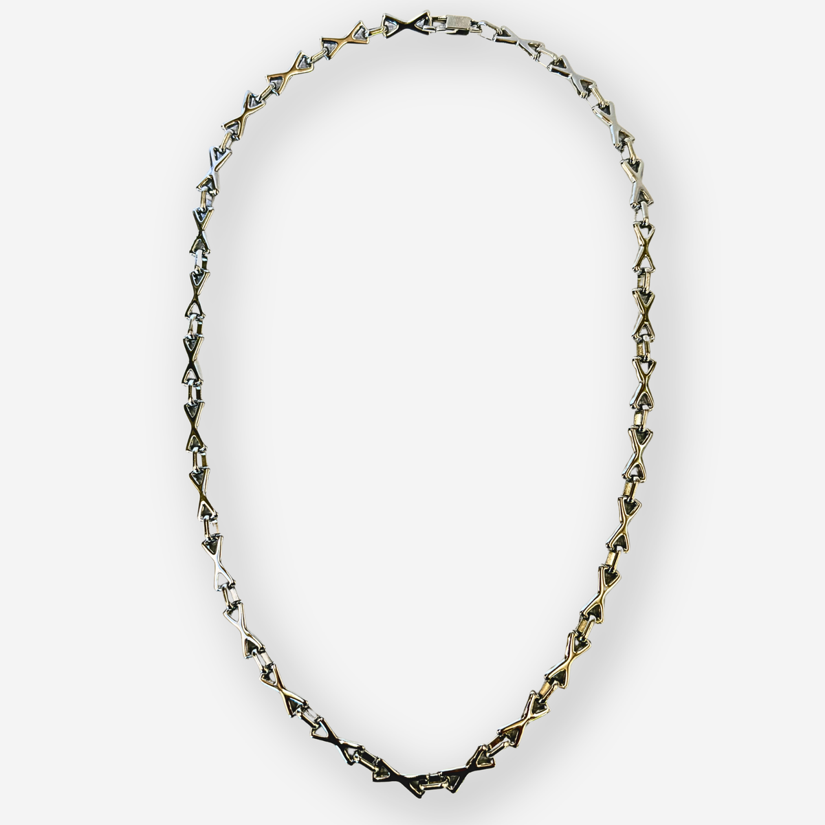 A silver-toned geometric chain necklace with triangular links, displayed in an oval shape against a light gray background.
