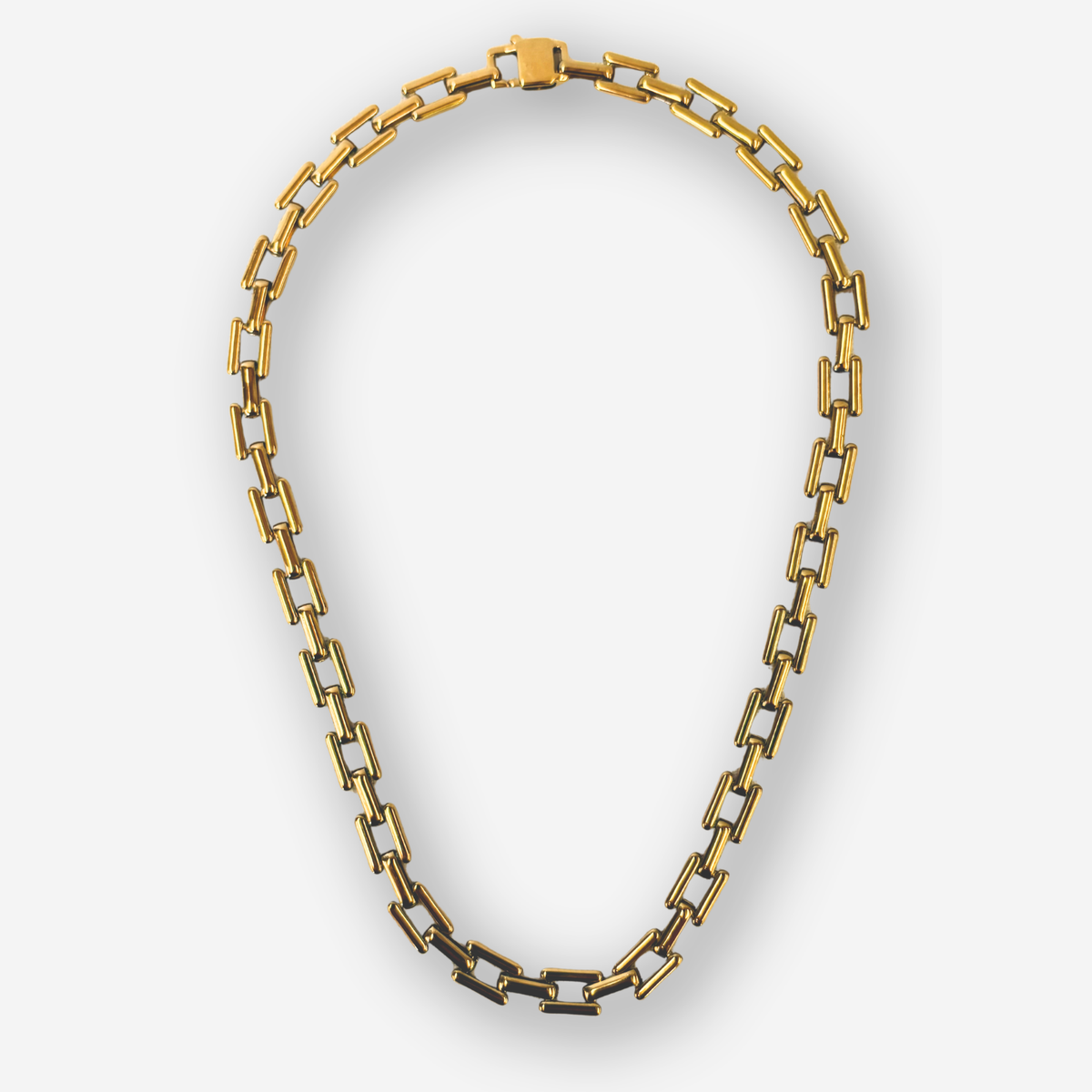 A gold-toned chain necklace with elongated rectangular links, arranged in an oval shape against a light gray background.