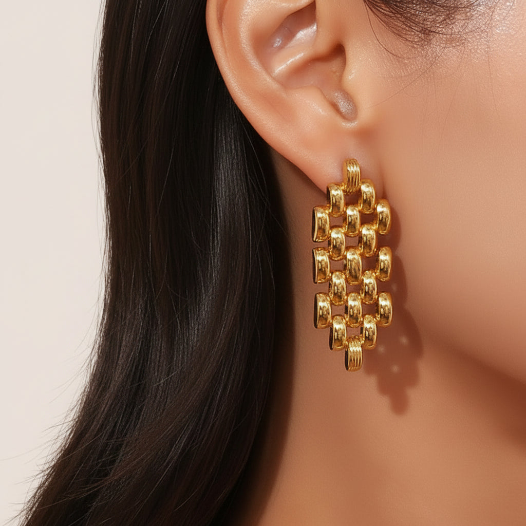 Gold chain link earrings being worn on an ear with a neutral background