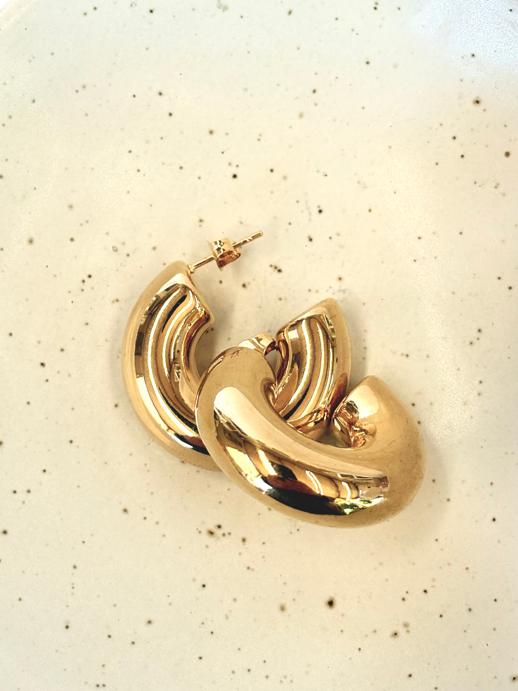 Gold hoop earrings on a speckled beige background