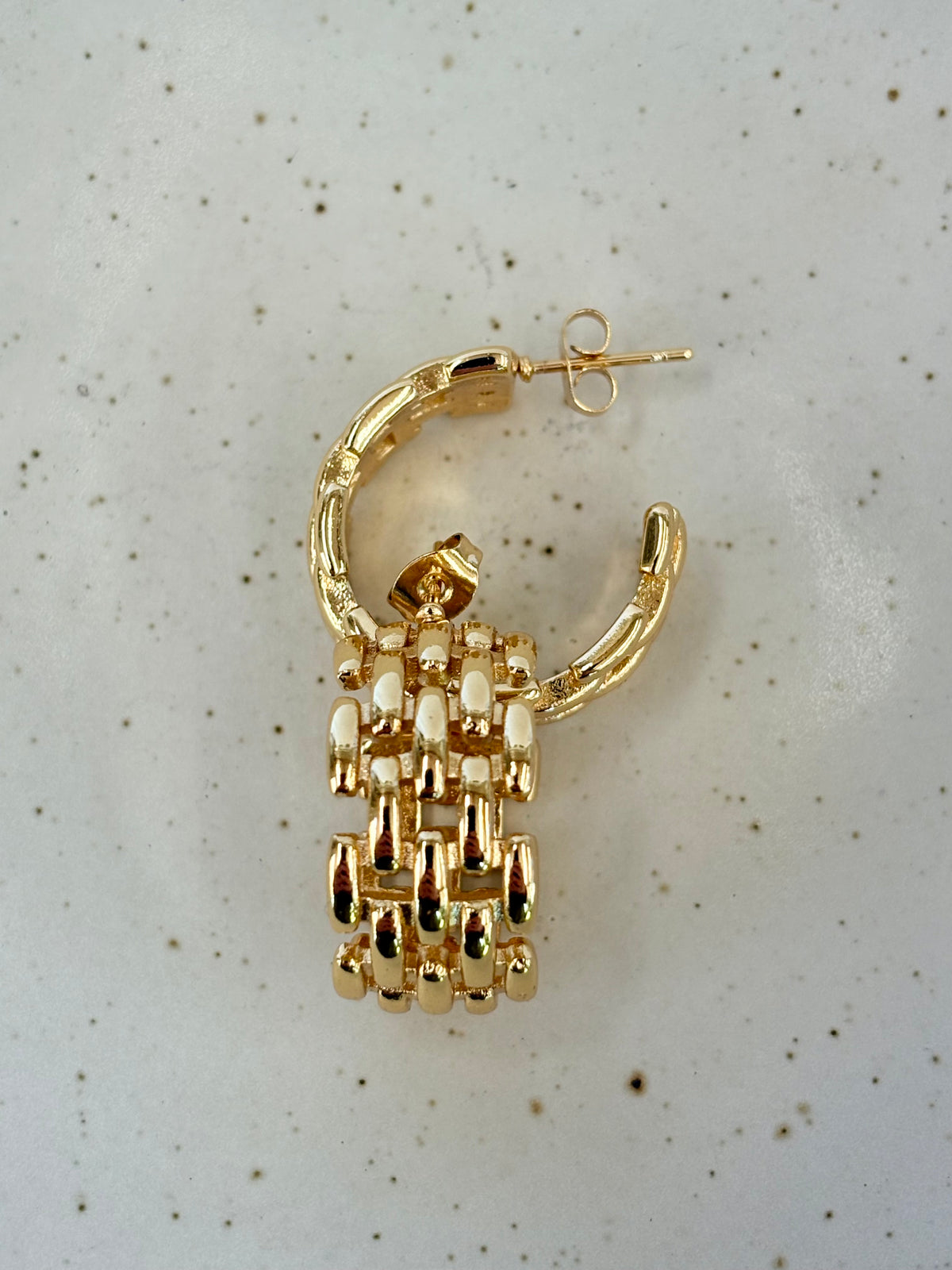 Gold hoop earring with chain detail on a speckled gray background