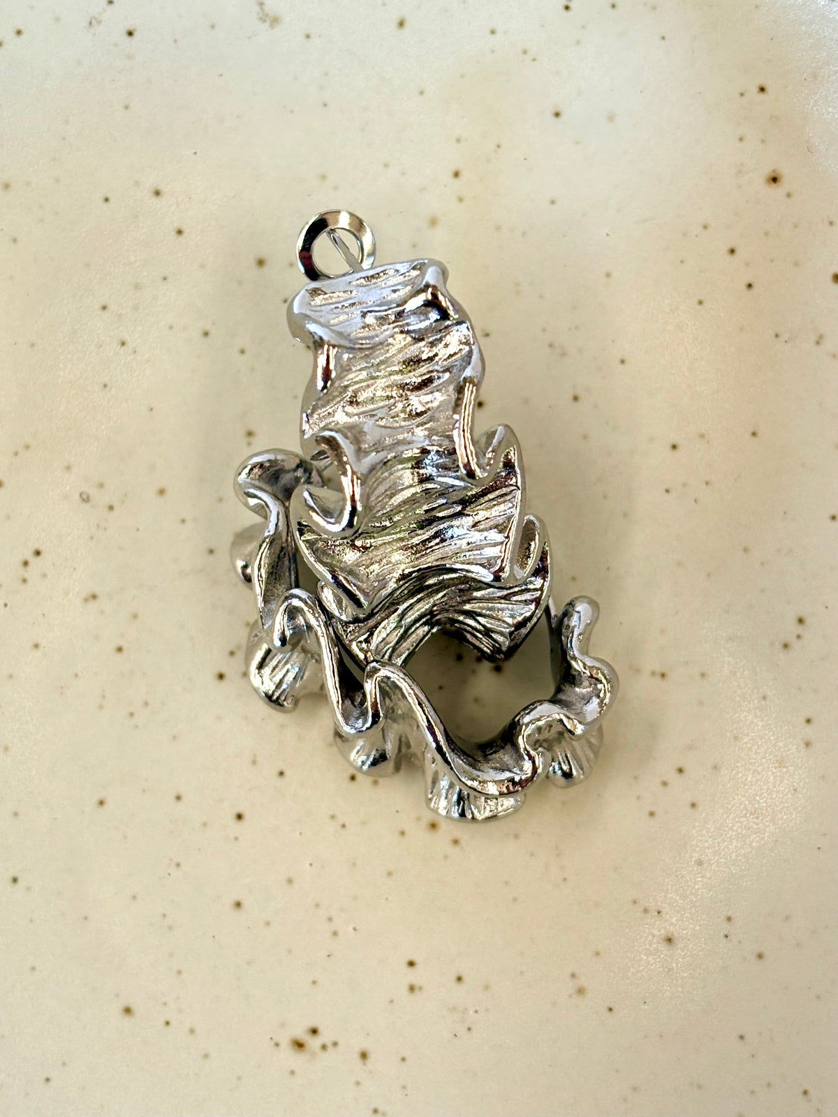 Silver crinkle earrings on a beige background