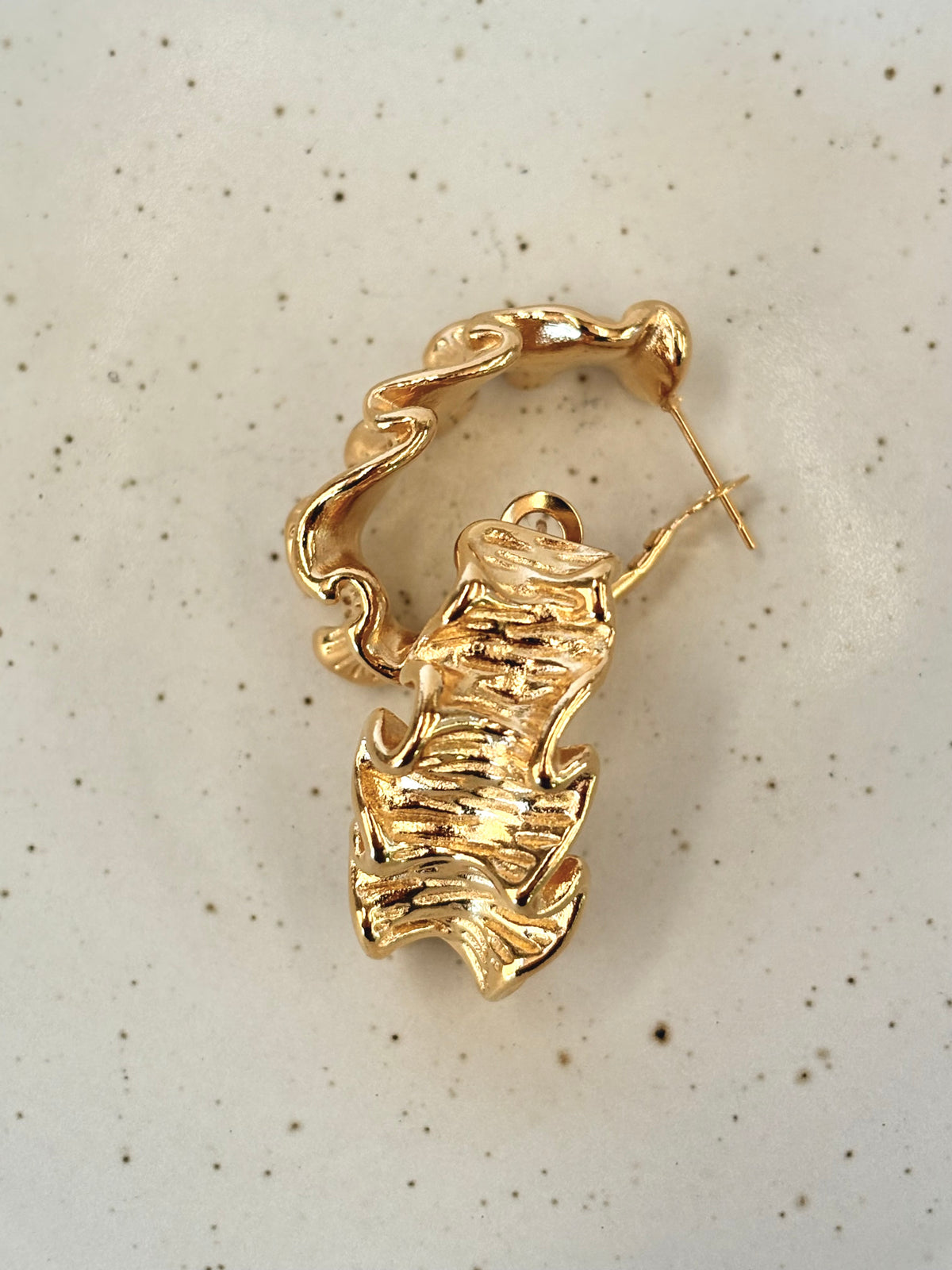 Gold leaf-shaped earring on a speckled beige background