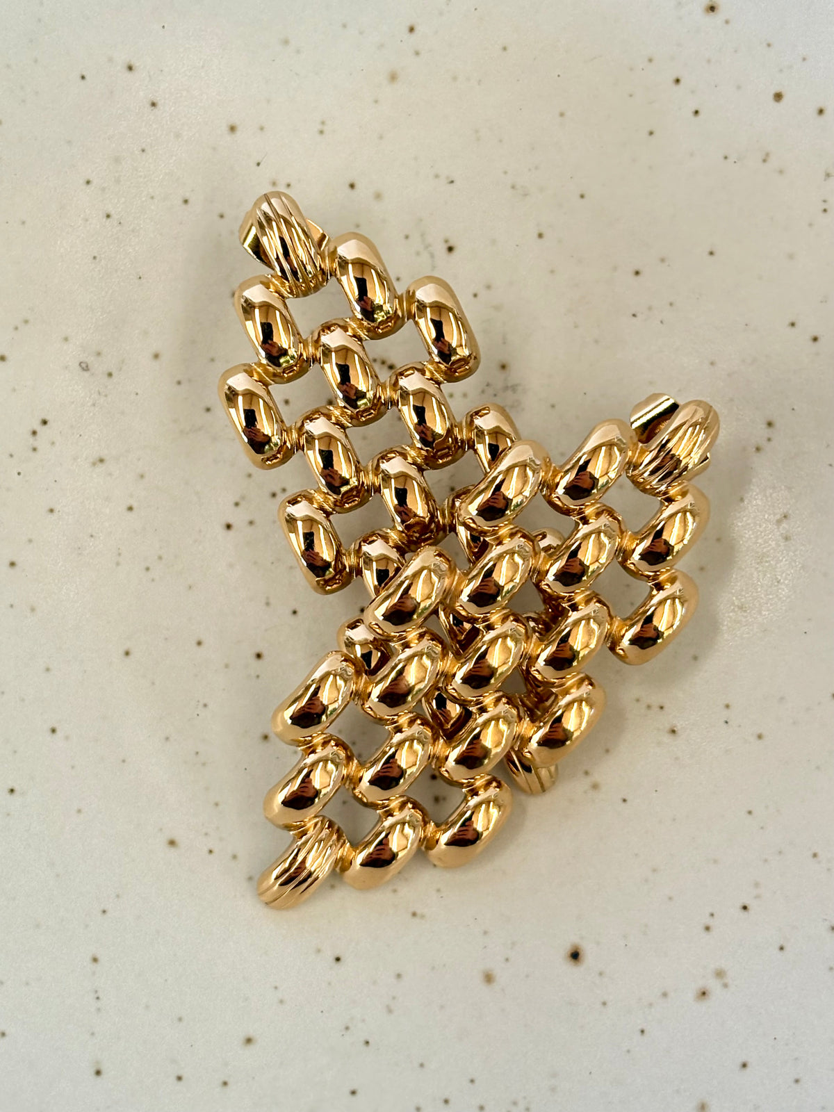 Gold chain link earrings on a textured beige background