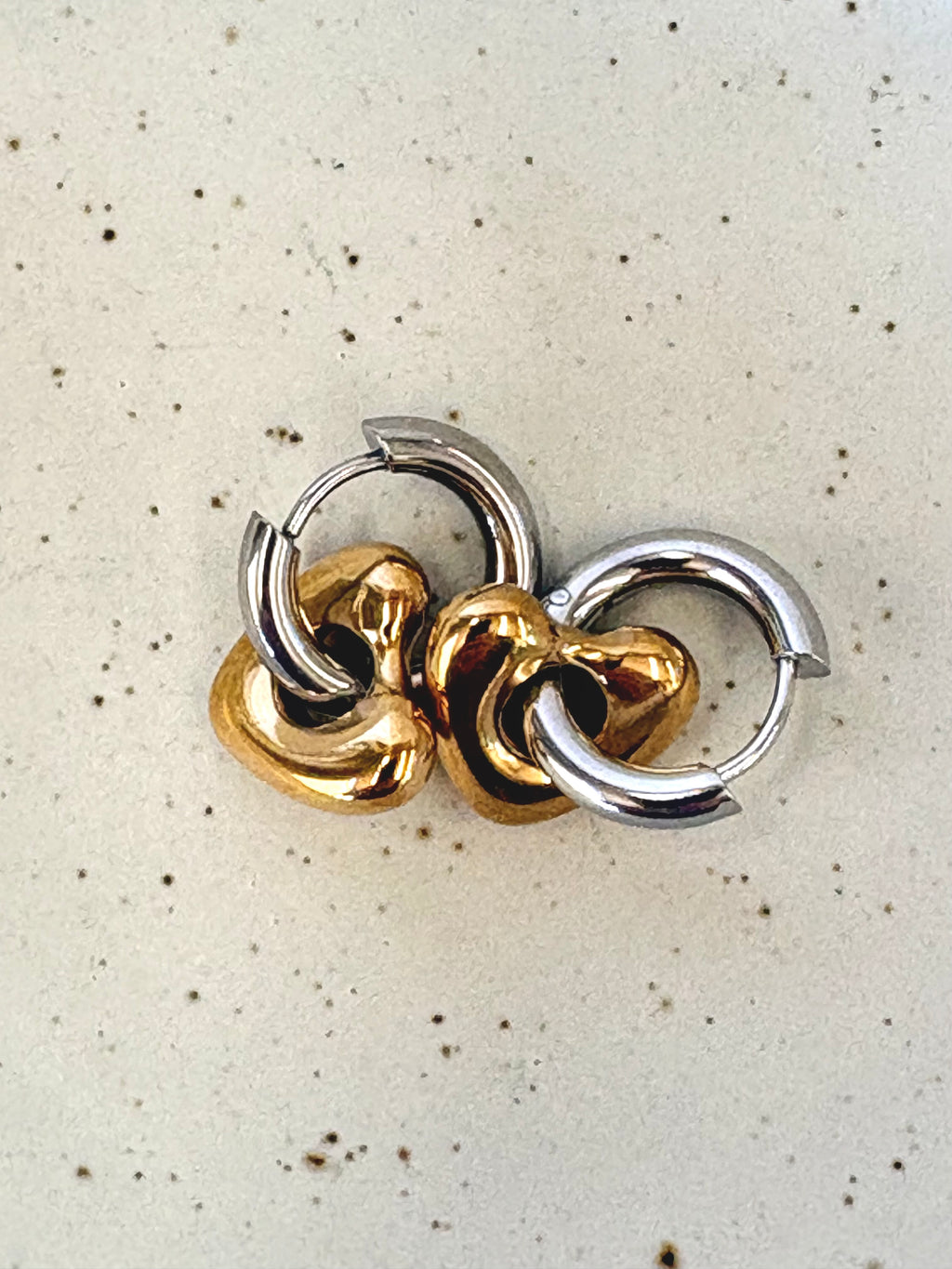 Pair of gold and silver hoop earrings on a speckled beige background