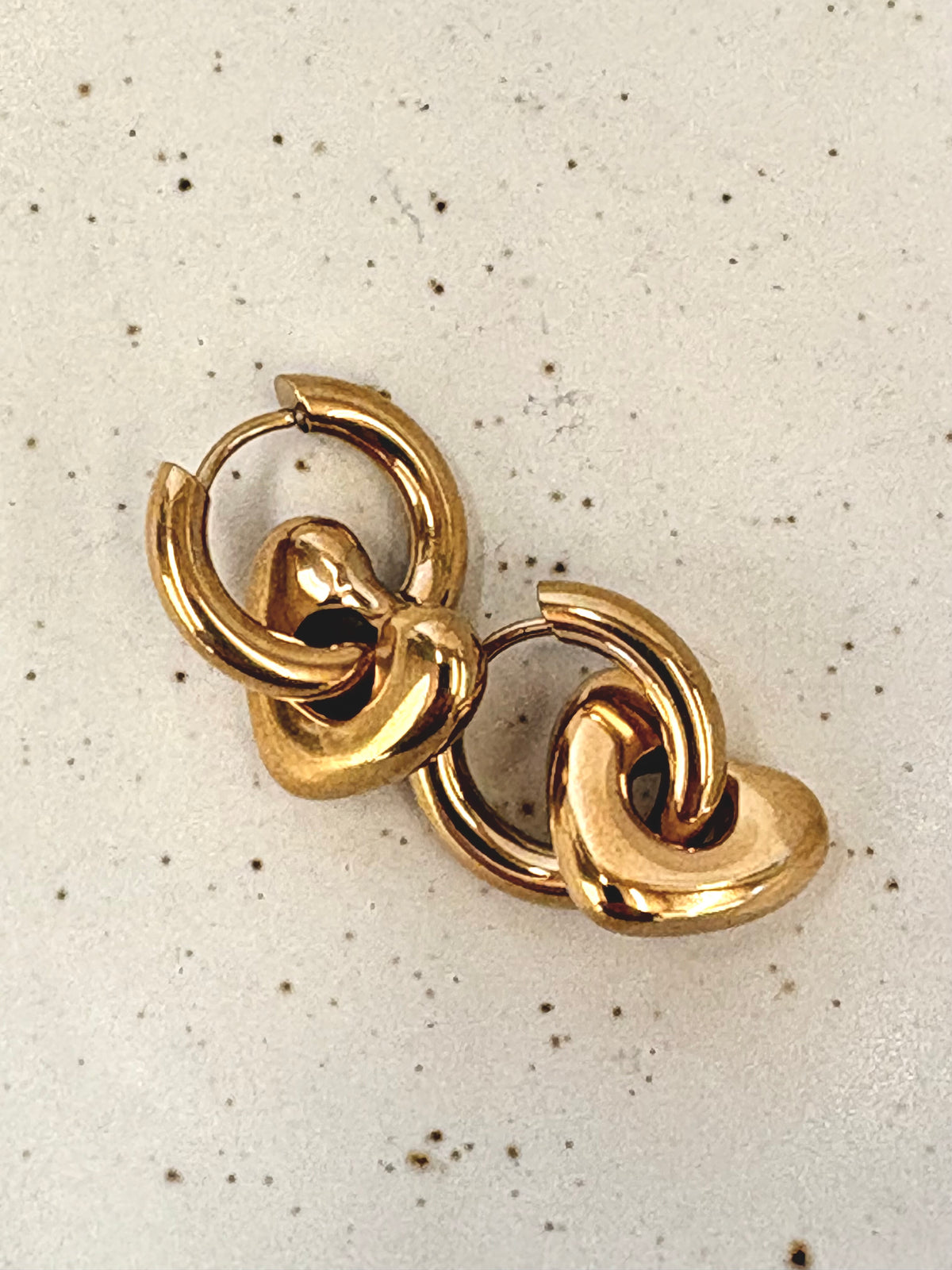 Gold hoop earrings on a speckled beige background