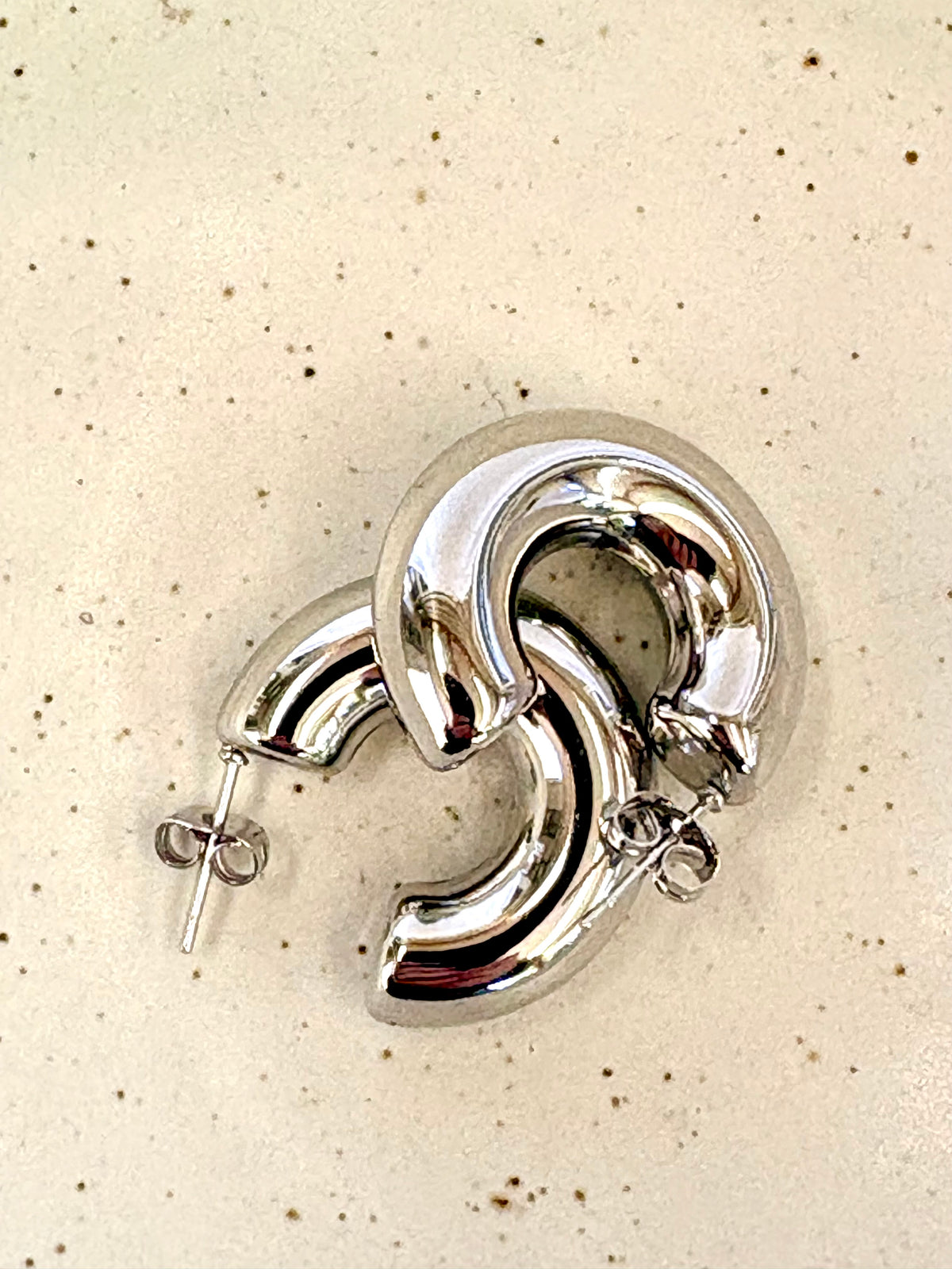 Silver hoop earrings on a beige speckled background