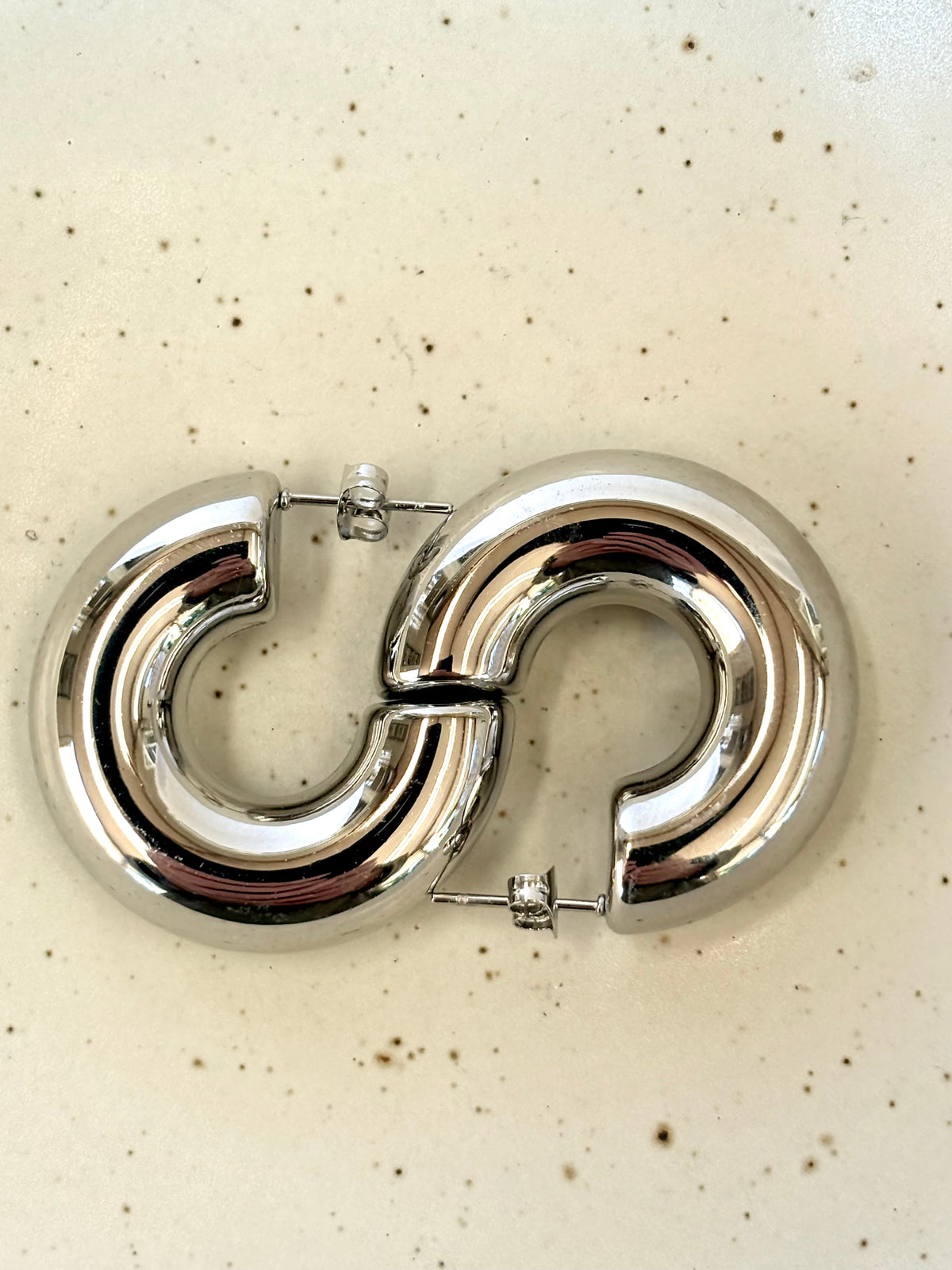 Silver hoop earring on a speckled beige background