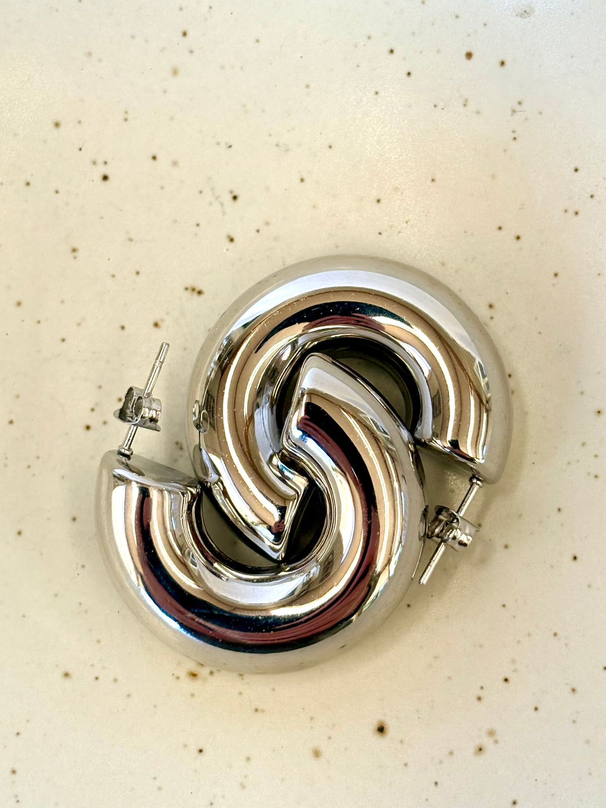 Silver large hoop earrings on a beige background