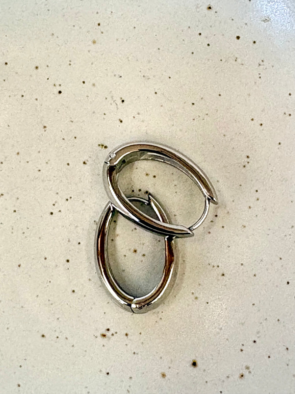 Pair of silver hoop earrings on a speckled beige surface