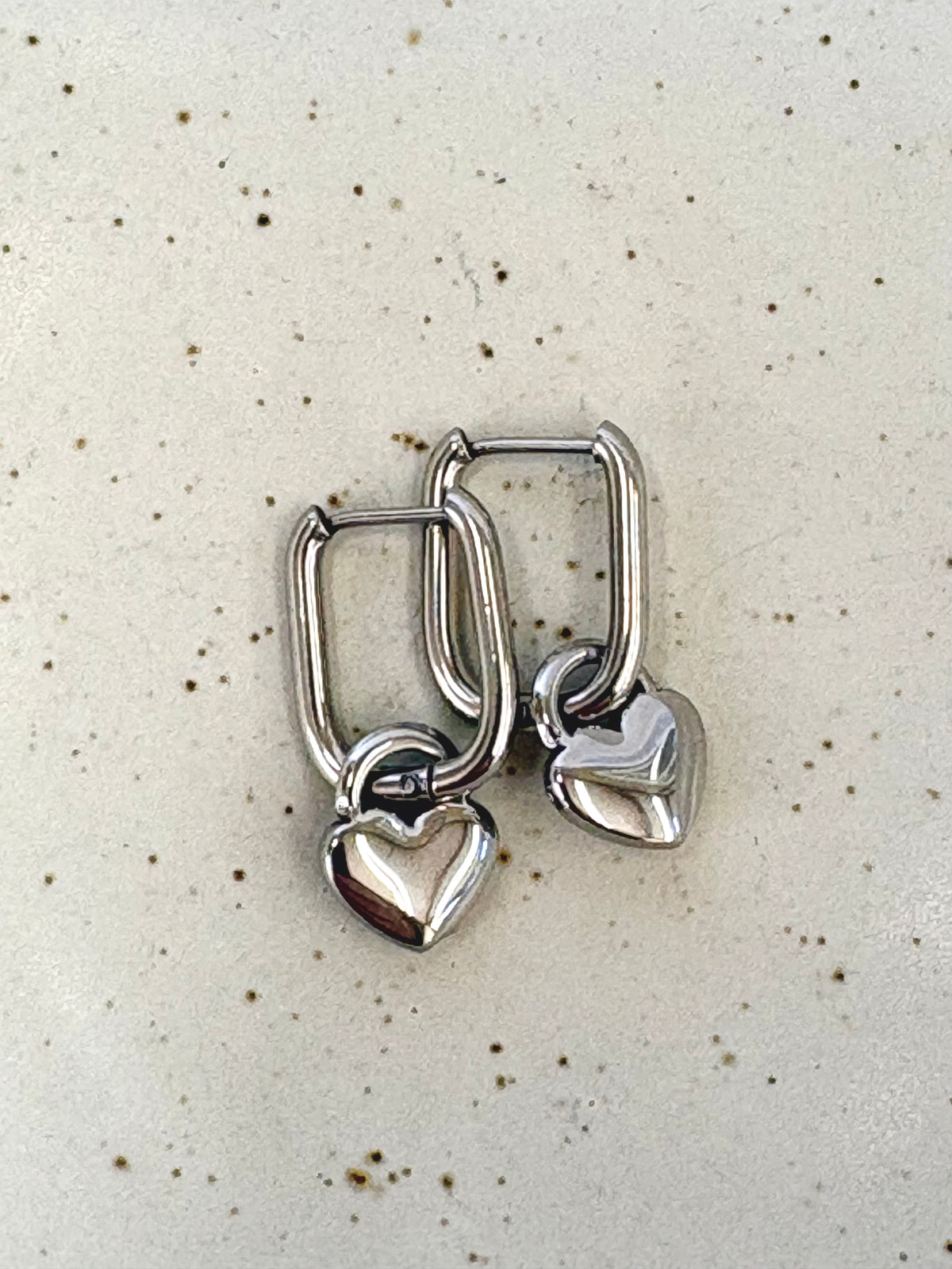 Pair of silver heart-shaped hoop earrings on a speckled beige background