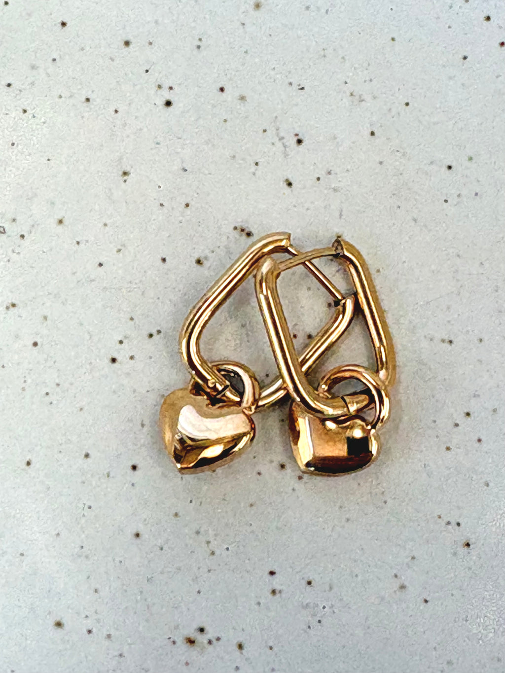 Gold heart-shaped earrings on a speckled gray background