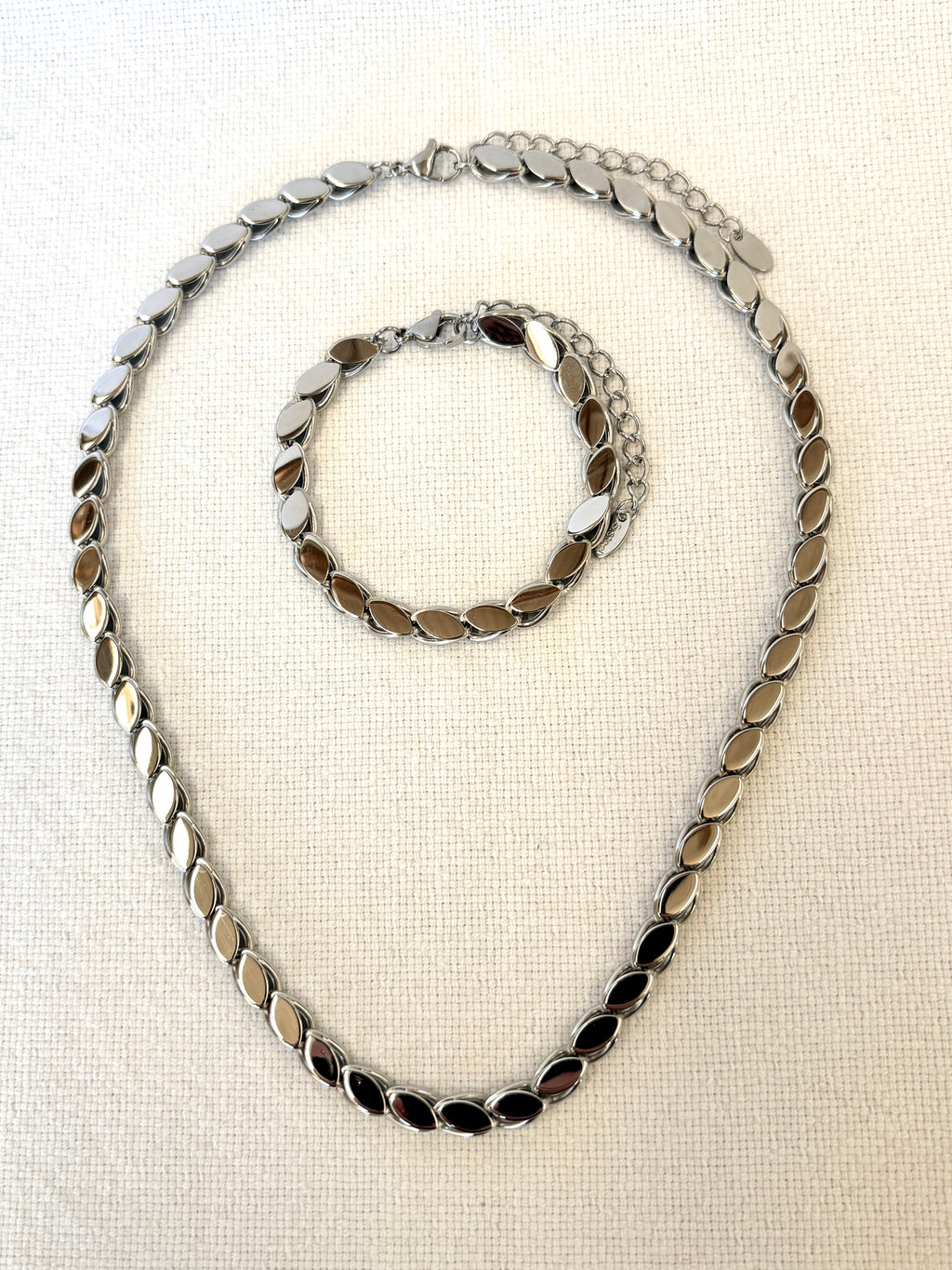 Silver chain necklace and bracelet on a beige fabric background