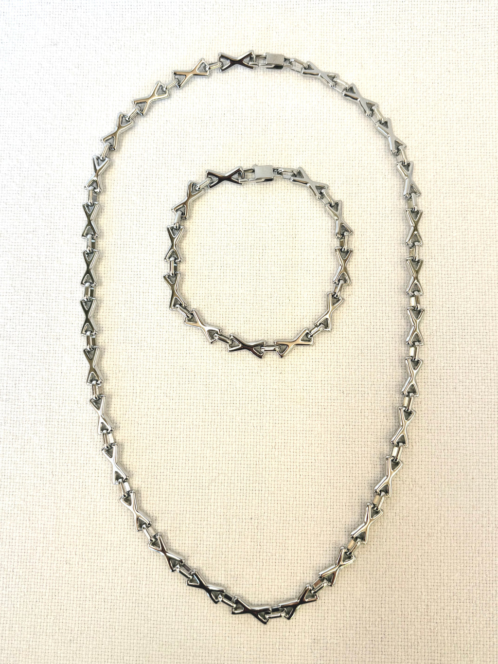 Silver necklace and bracelet set on a beige fabric background