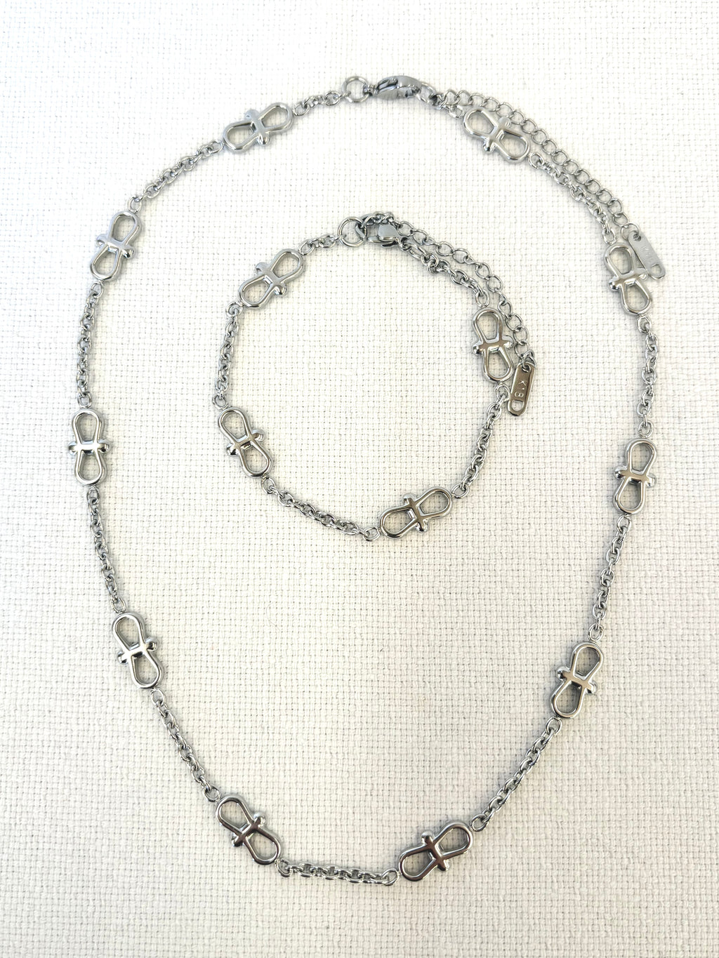 Infinity Chain Silver Bracelet and necklace on textured white background
