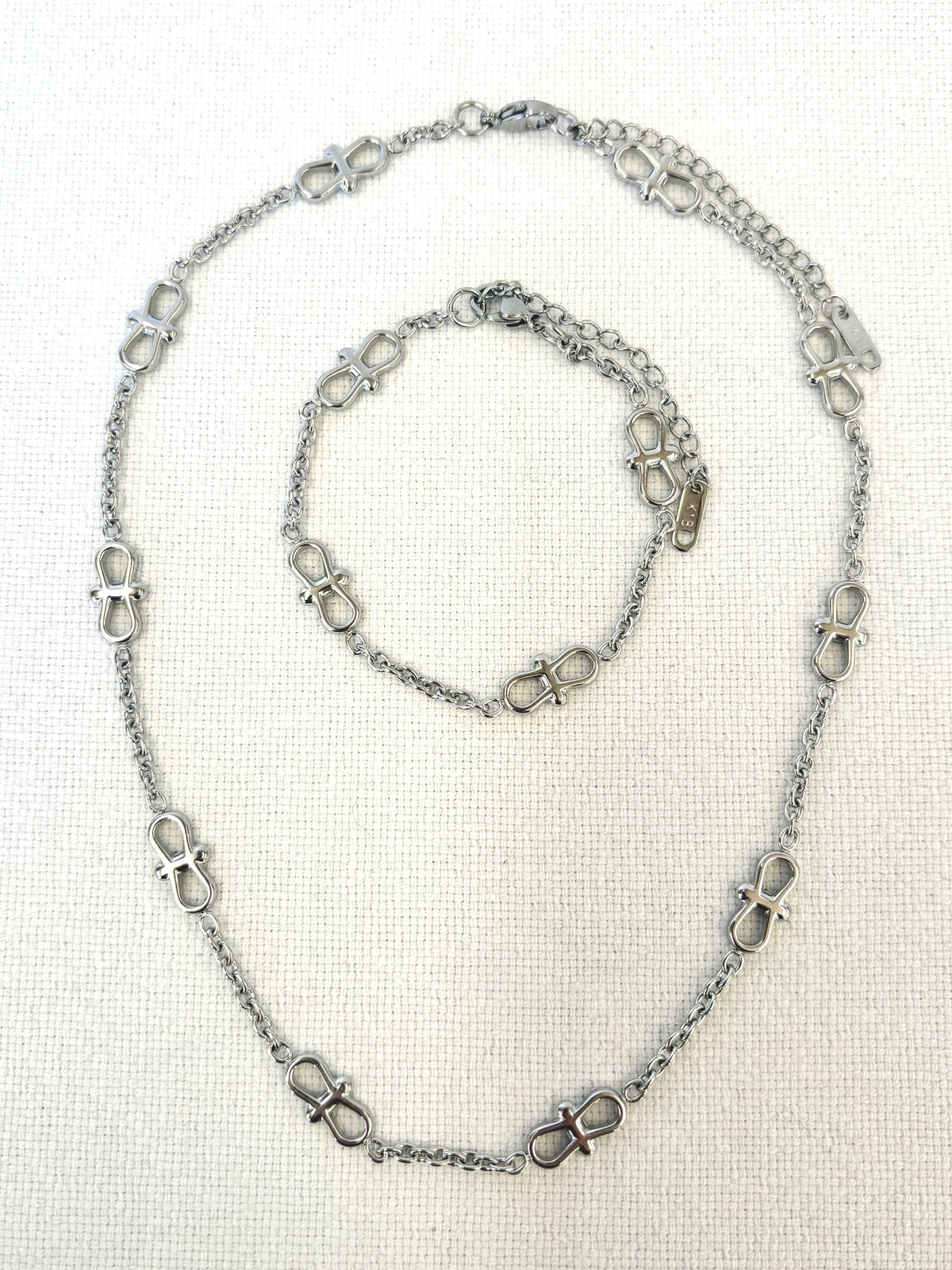 Infinity Chain Silver Bracelet and necklace on textured white background
