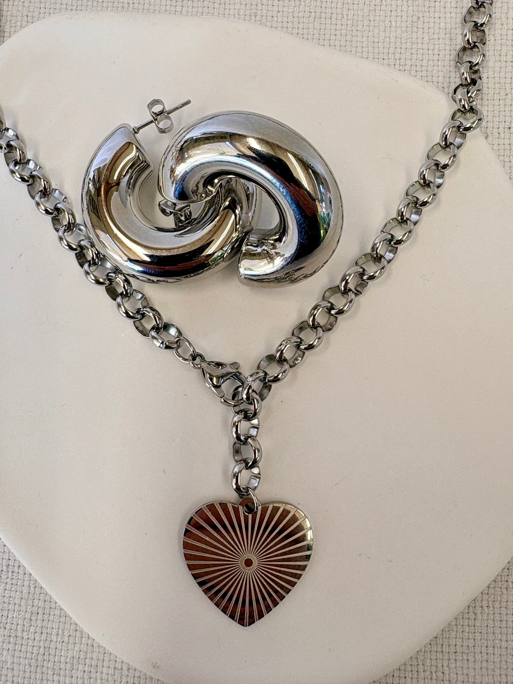 Silver necklace with a heart pendant and earrings on a white stand.