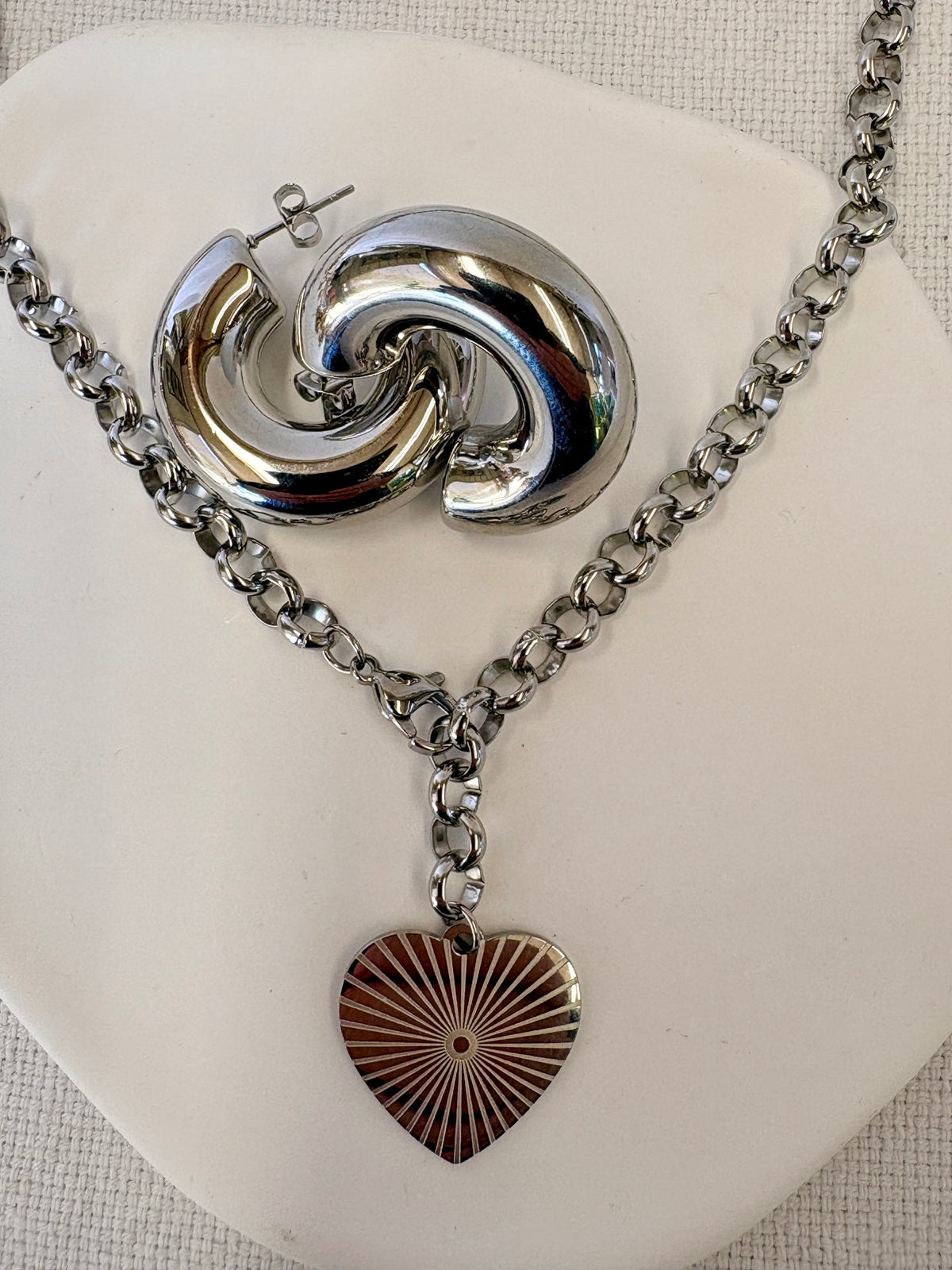 Silver necklace with a heart pendant and earrings on a white stand.