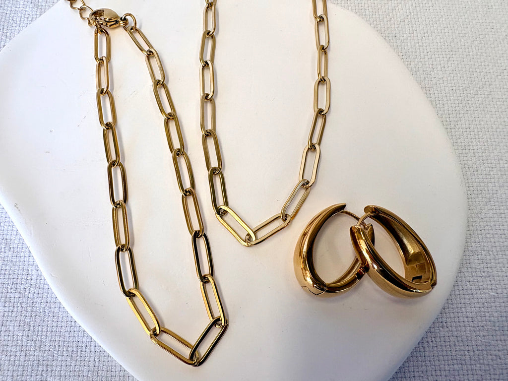 Gold chain necklace and hoop earrings on a white plate with a light gray background