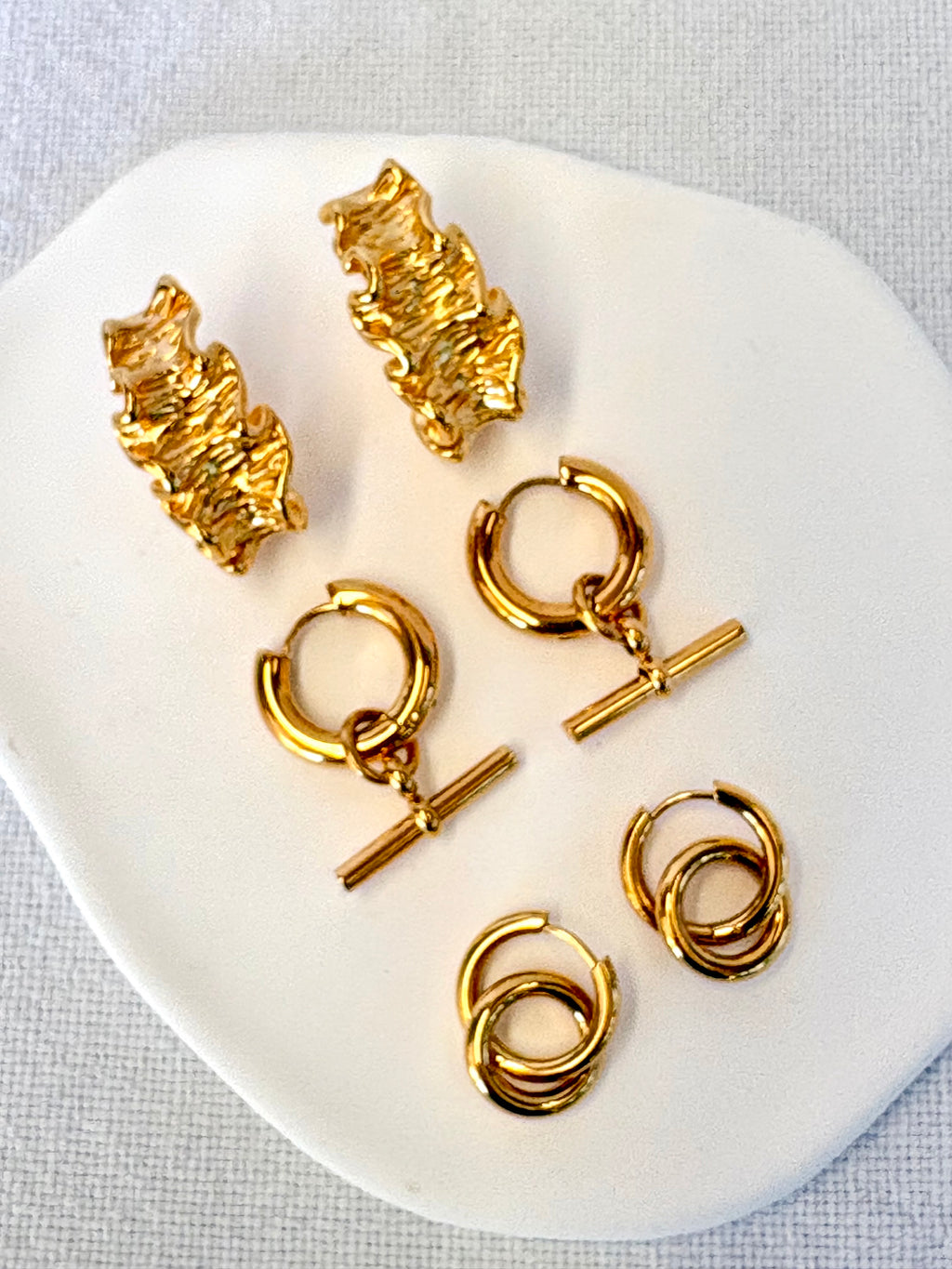 Set of gold earrings on a white dish with a light gray background