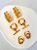 Set of gold earrings on a white dish with a light gray background