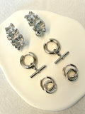 Set of silver earrings on a white stand with a beige fabric background