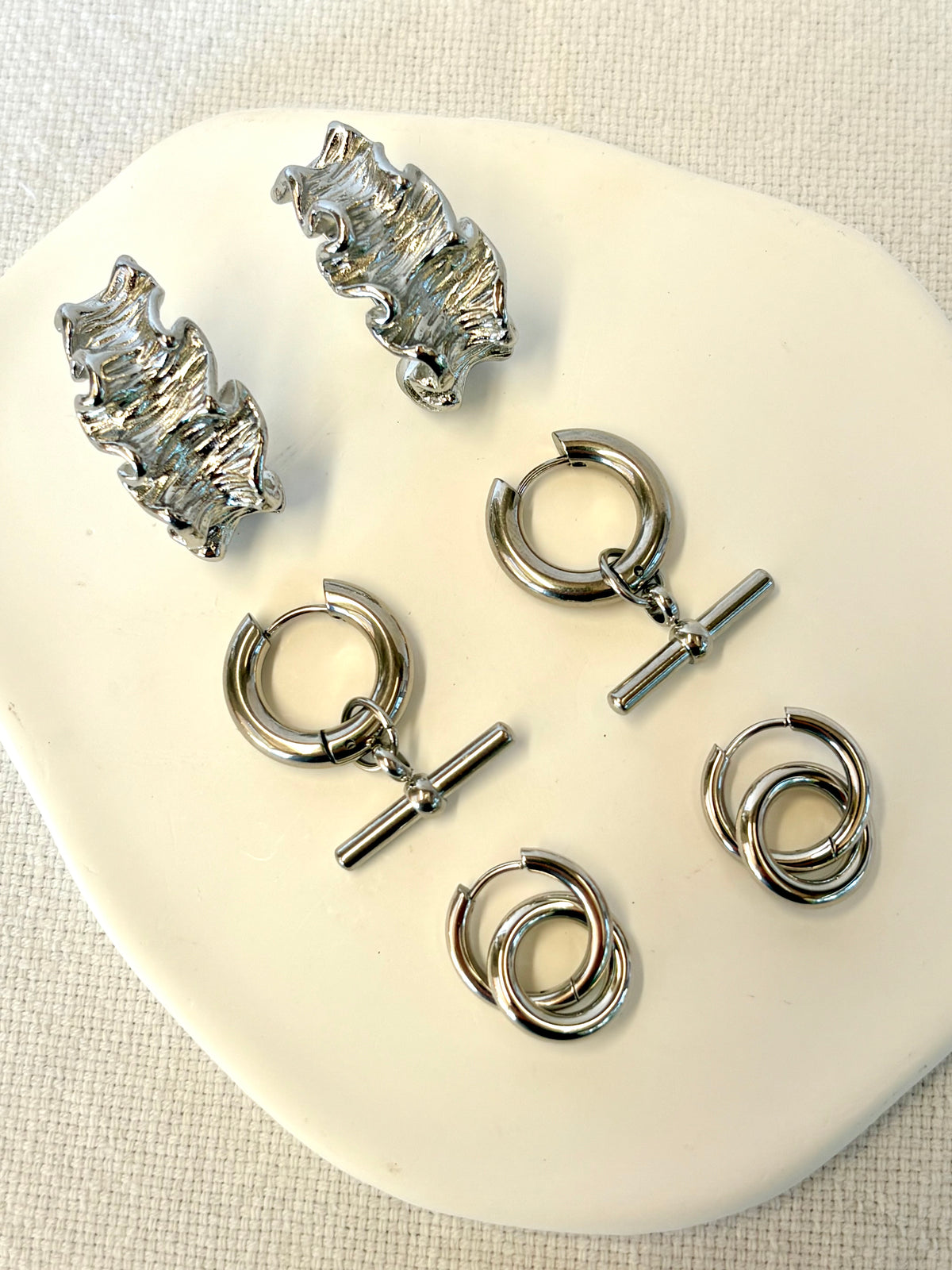 Set of silver earrings on a white stand with a beige fabric background