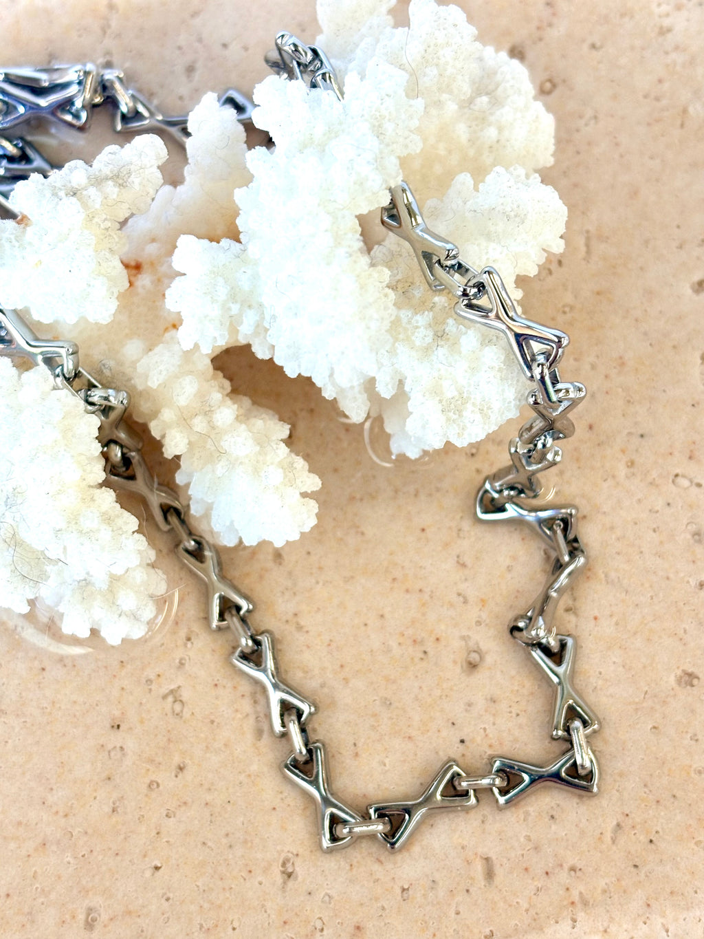Silver necklace with geometric design on a beige background