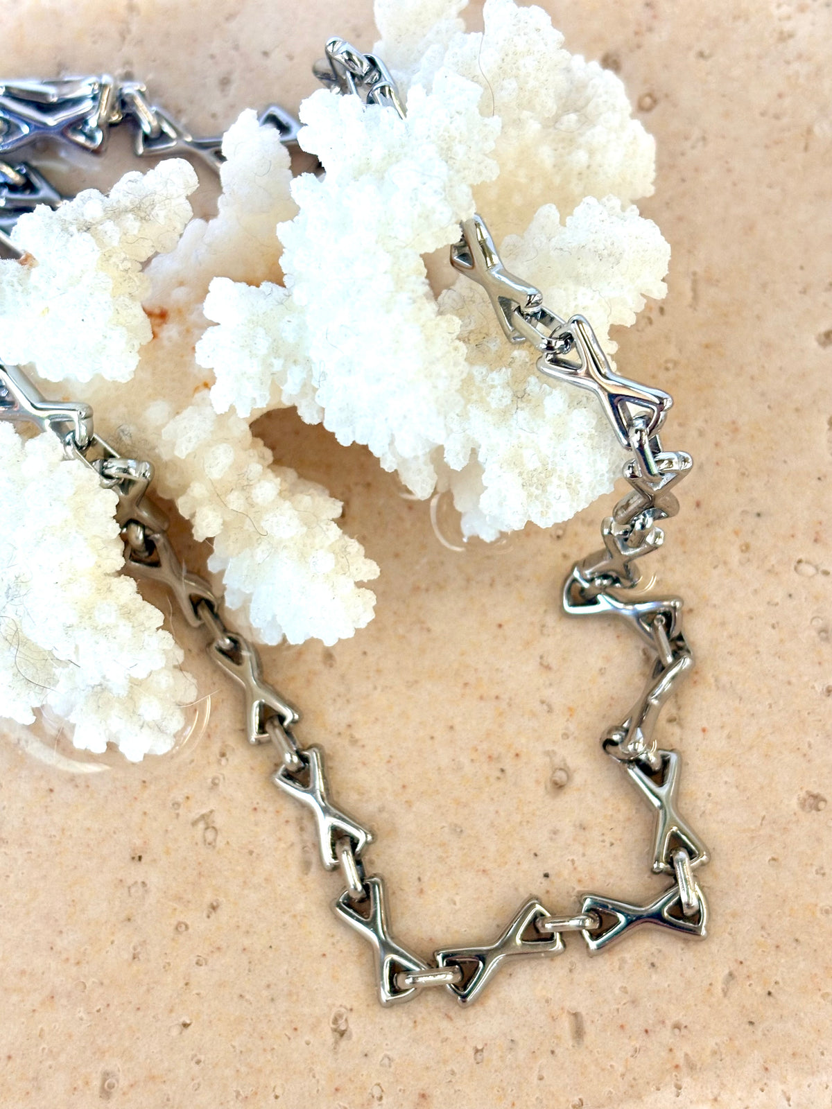 Silver necklace with geometric design on a beige background