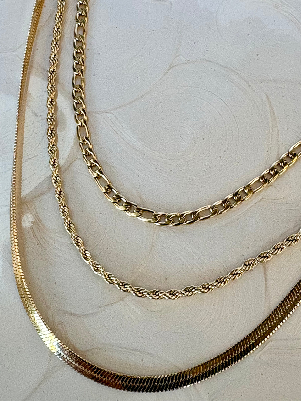 Three gold chains of different styles on a light marble surface