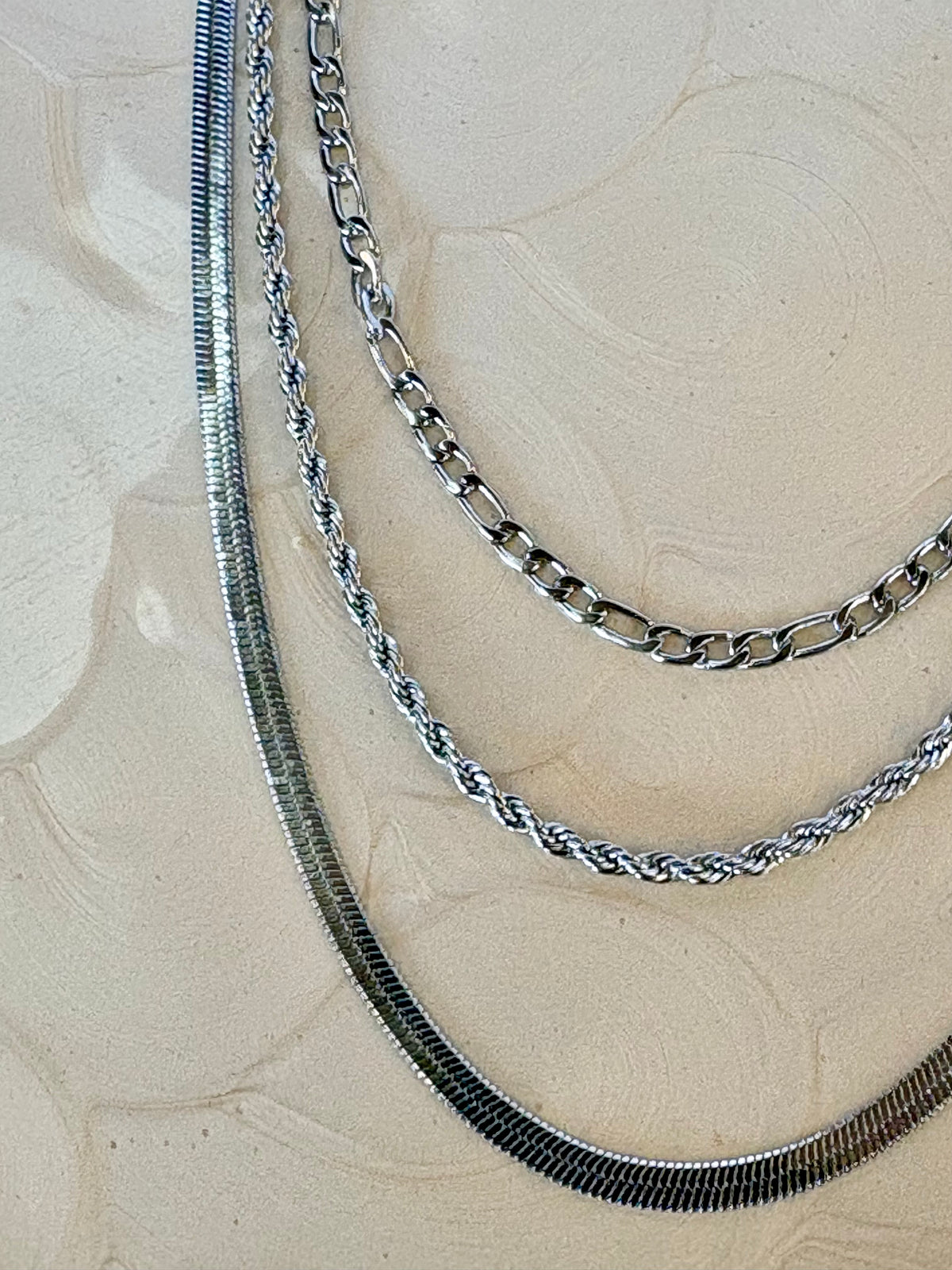 Three silver chains of different styles on a textured beige surface
