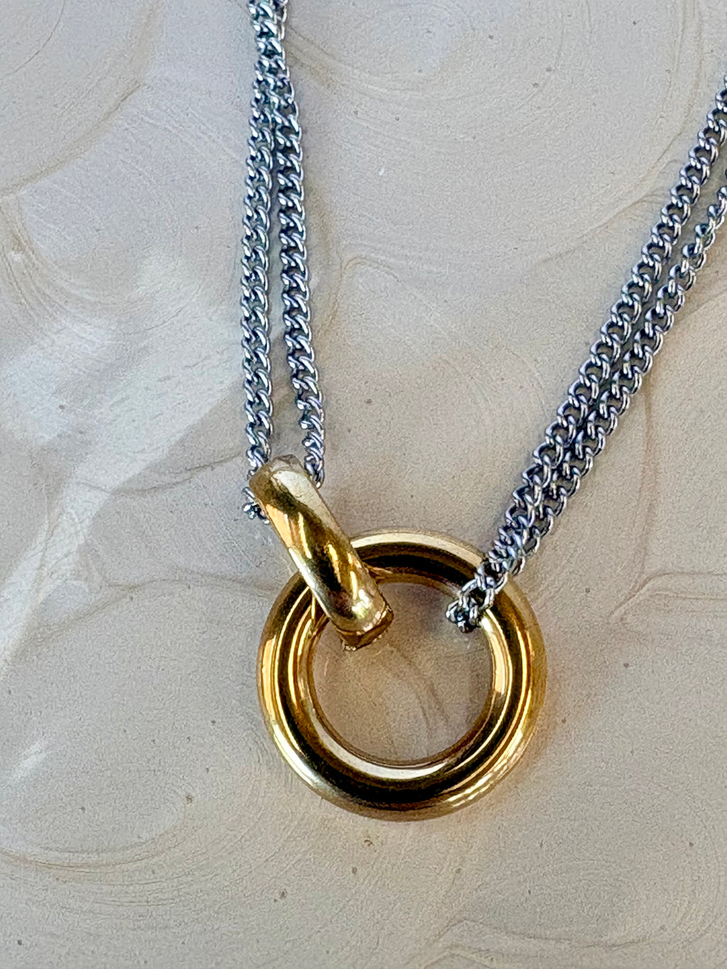 Gold ring pendant on a silver chain against a textured beige background