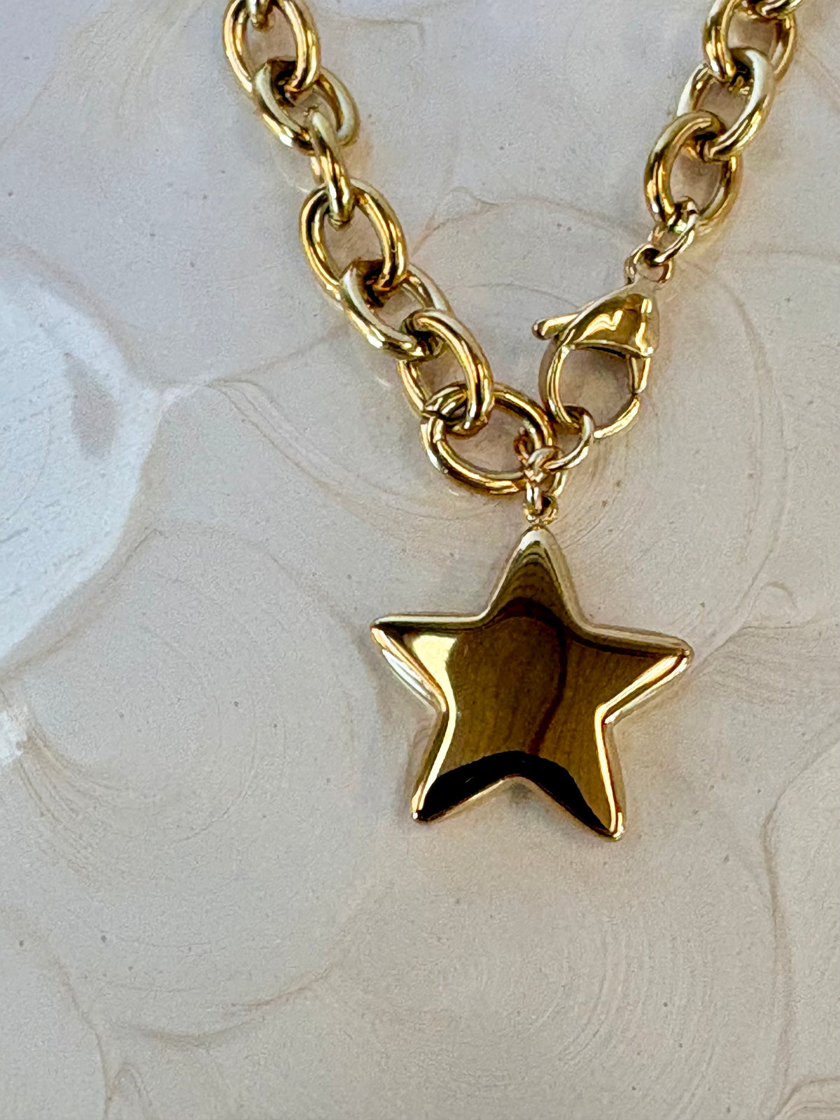 Gold chain necklace with a star pendant on a textured white background