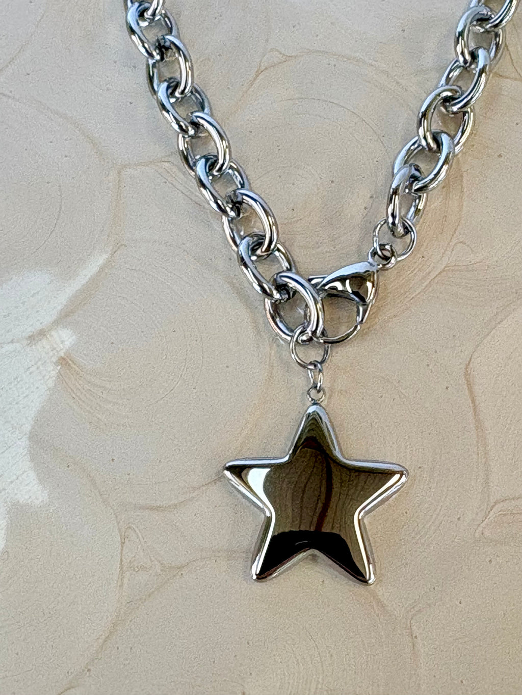 Silver chain necklace with a star-shaped pendant on a beige textured background