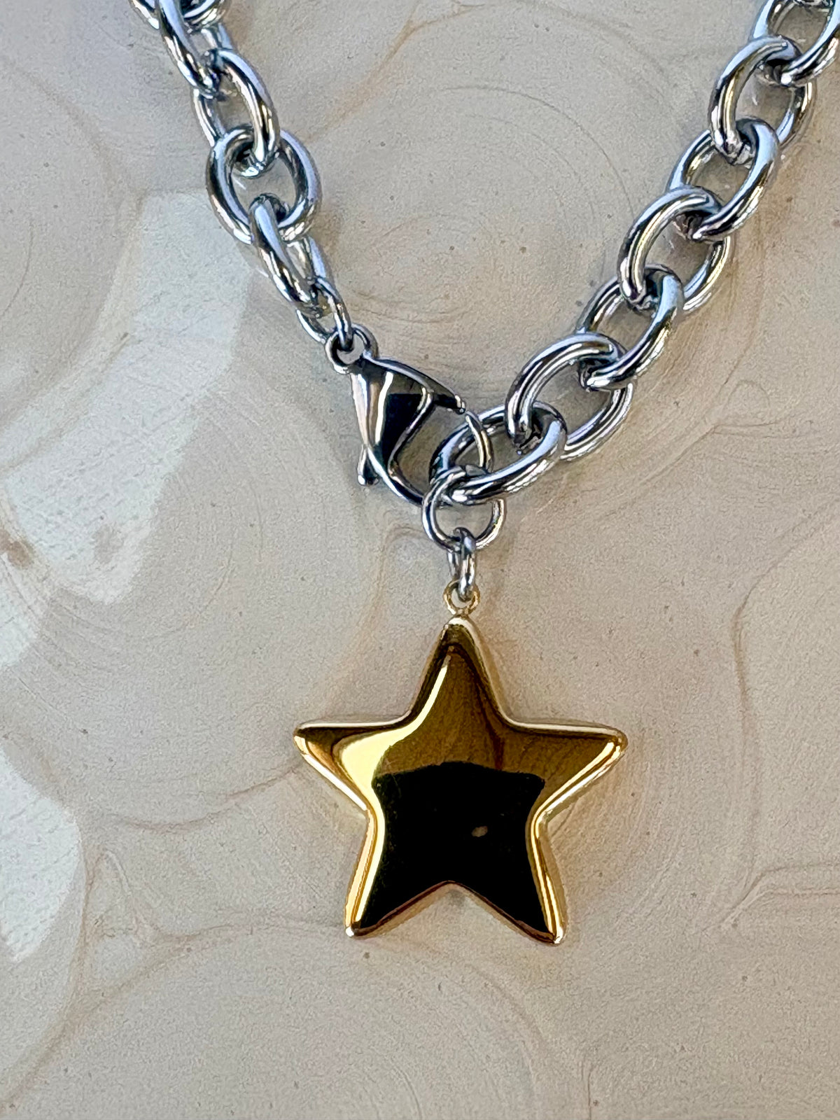 Silver chain necklace with a gold star pendant on a textured beige background