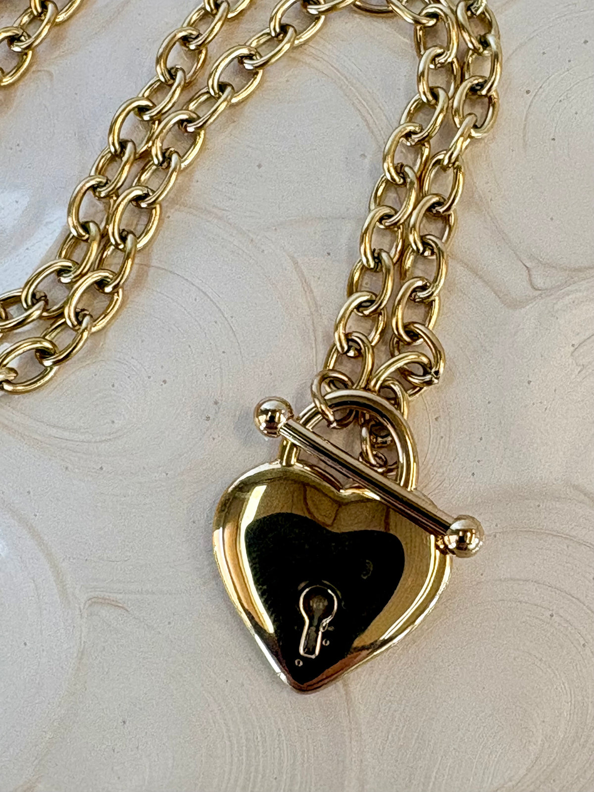 Gold heart-shaped padlock on a chain against a light background