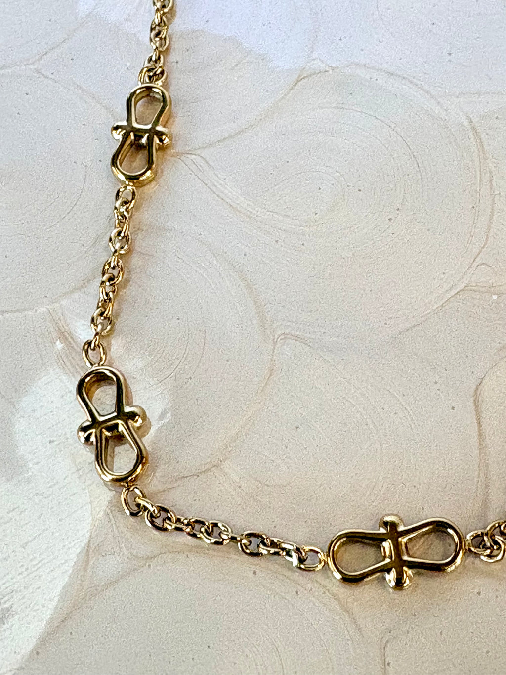 Gold chain bracelet with infinity shaped links on a textured beige background