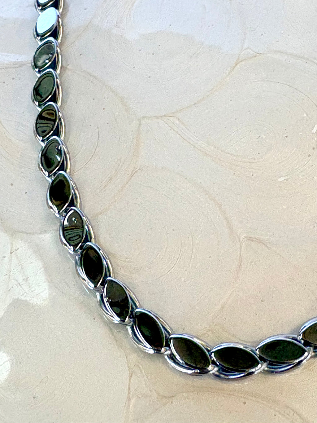 Silver Necklace with overlapping leaf pattern on a beige background