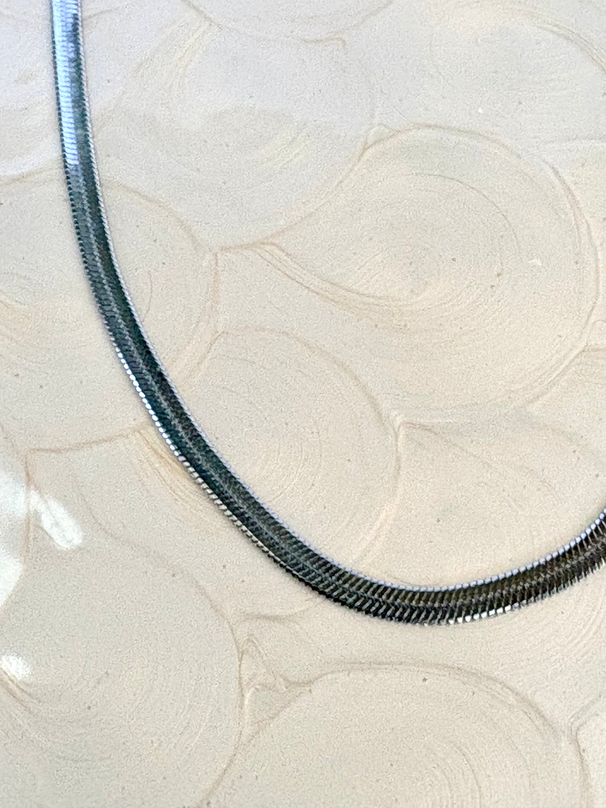Silver herringbone chain on a textured beige background