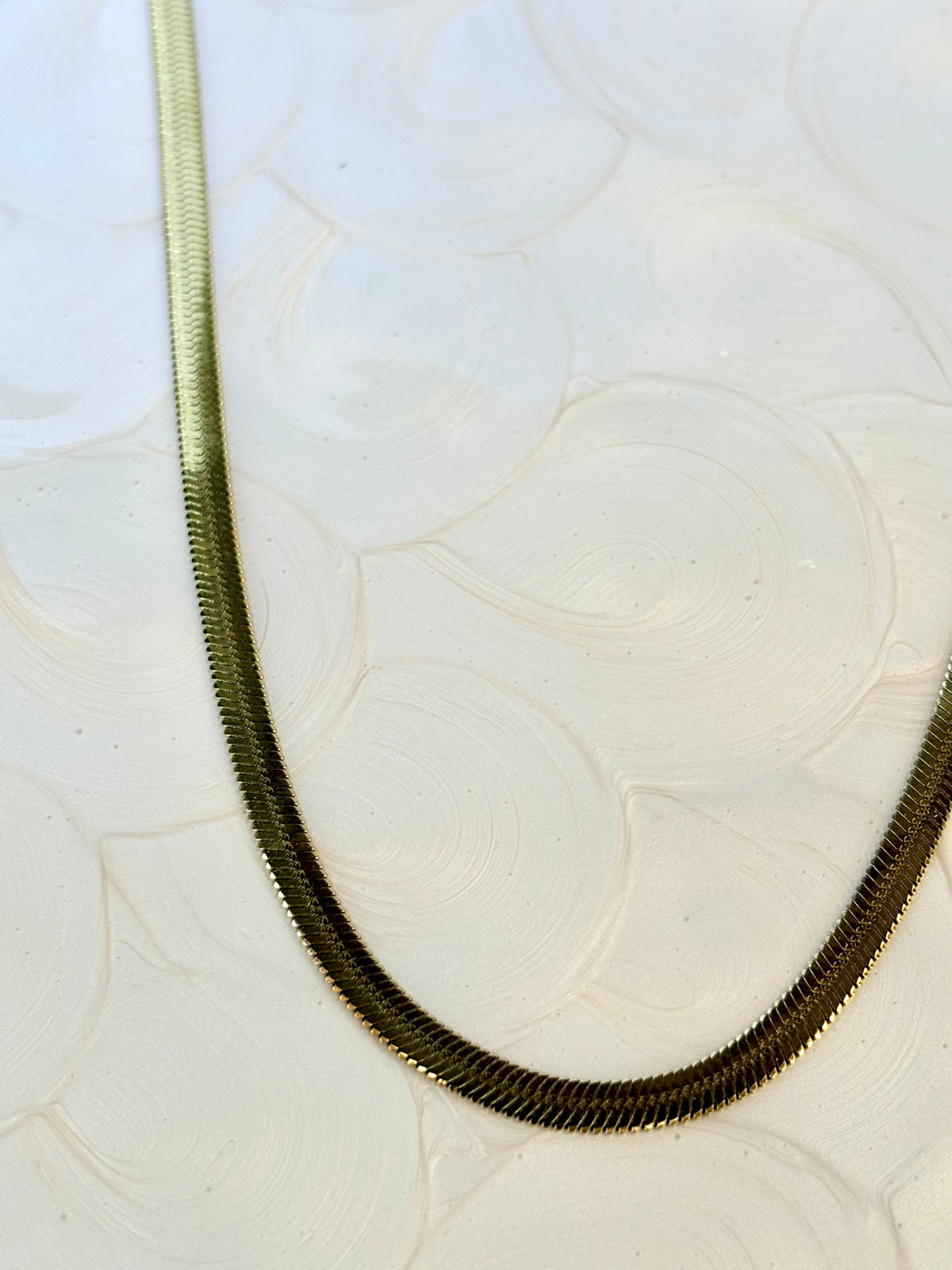 Long herringbone chain necklace on a textured white surface