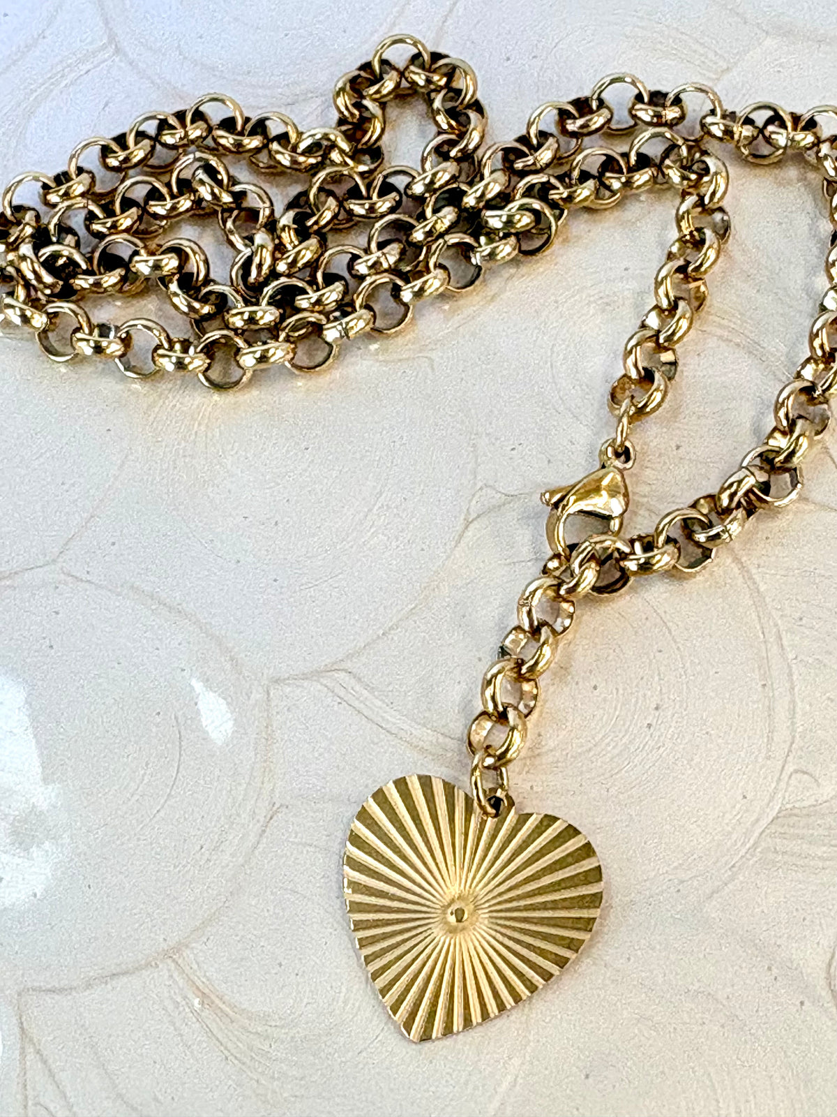 Gold chain necklace with a heart-shaped sunburst pendant on a light background
