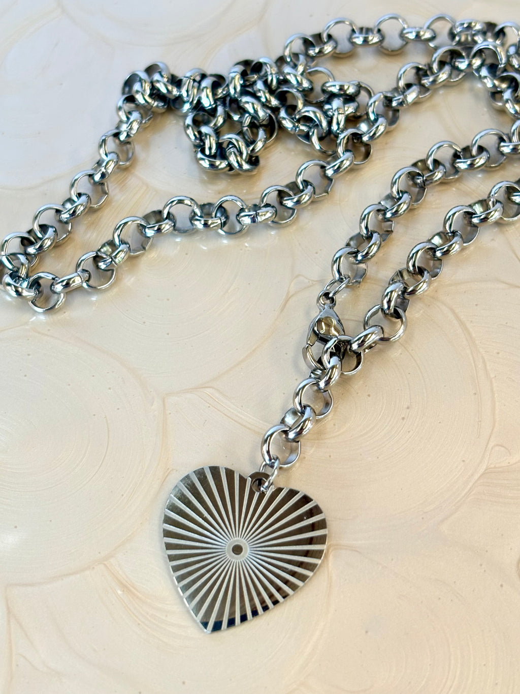 Silver chain necklace with a heart-shaped sunburst pendant on a textured beige surface