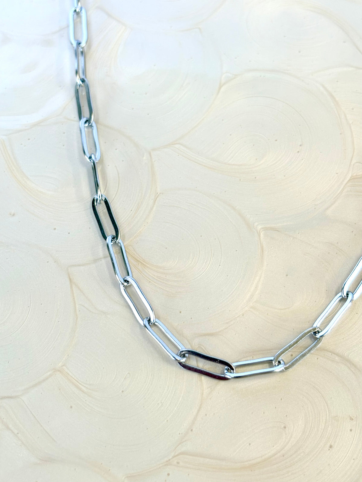 Silver chain necklace on a textured beige surface