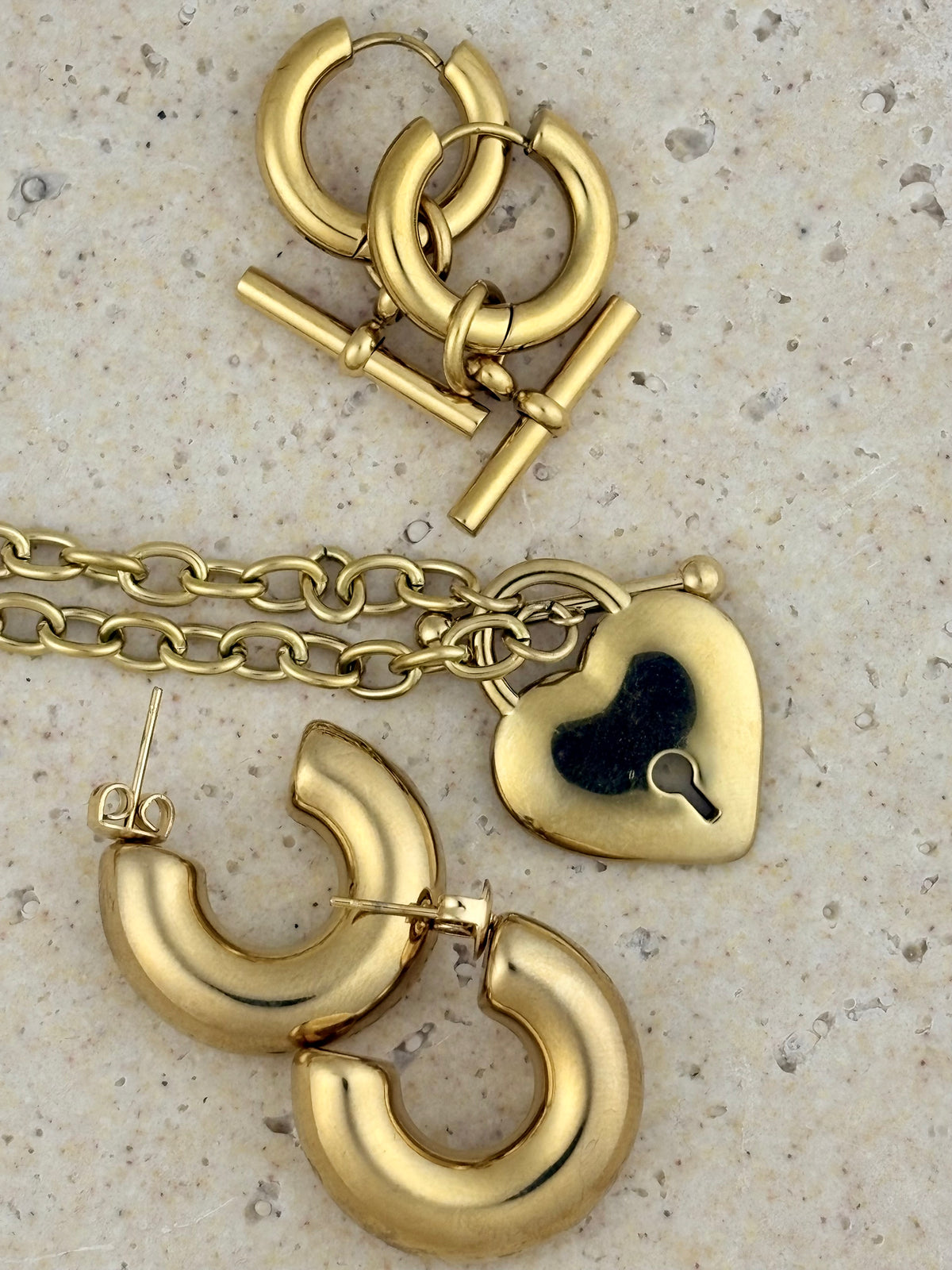 Gold hoop earrings and necklace set on a textured beige surface