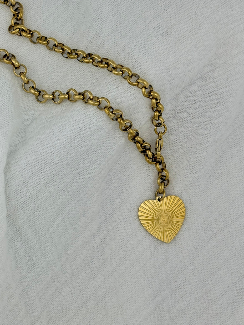Gold chain necklace with a heart-shaped pendant on a light gray background