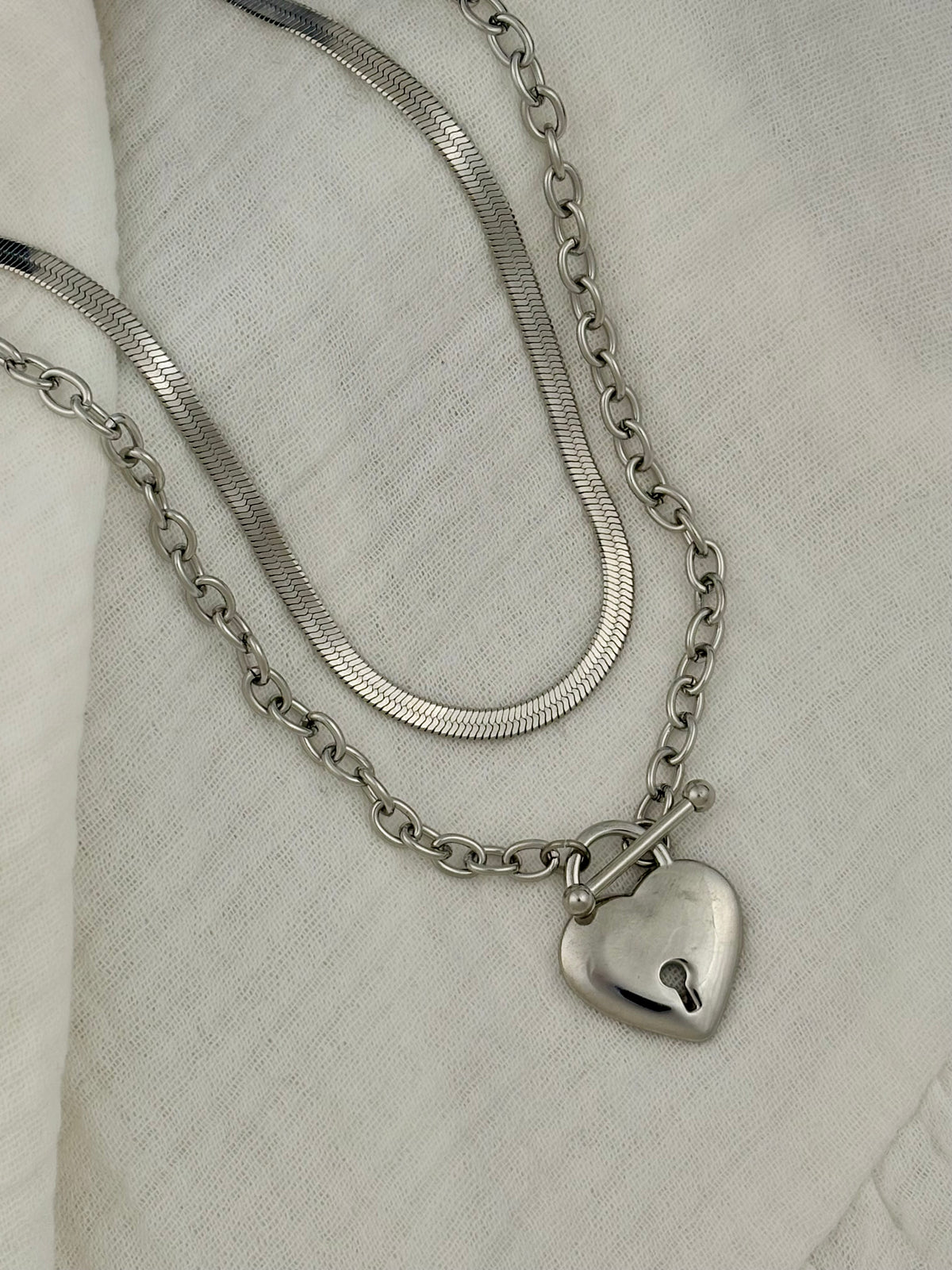 Silver chain necklace with a heart-shaped pendant on a light fabric background