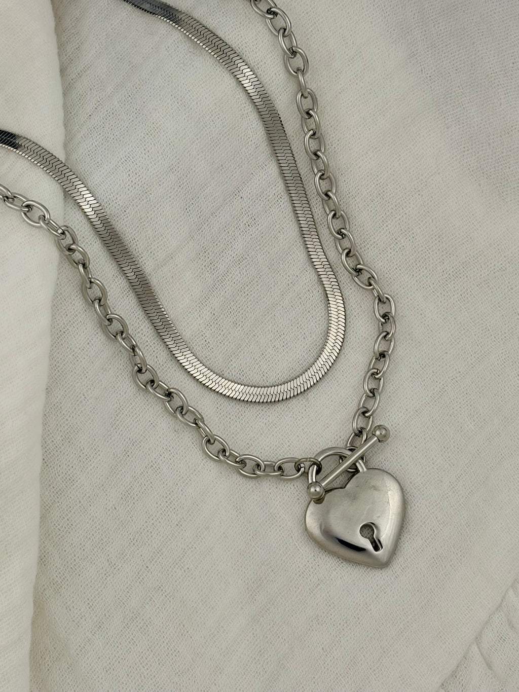 Silver chain necklace with a heart-shaped pendant on a light fabric background